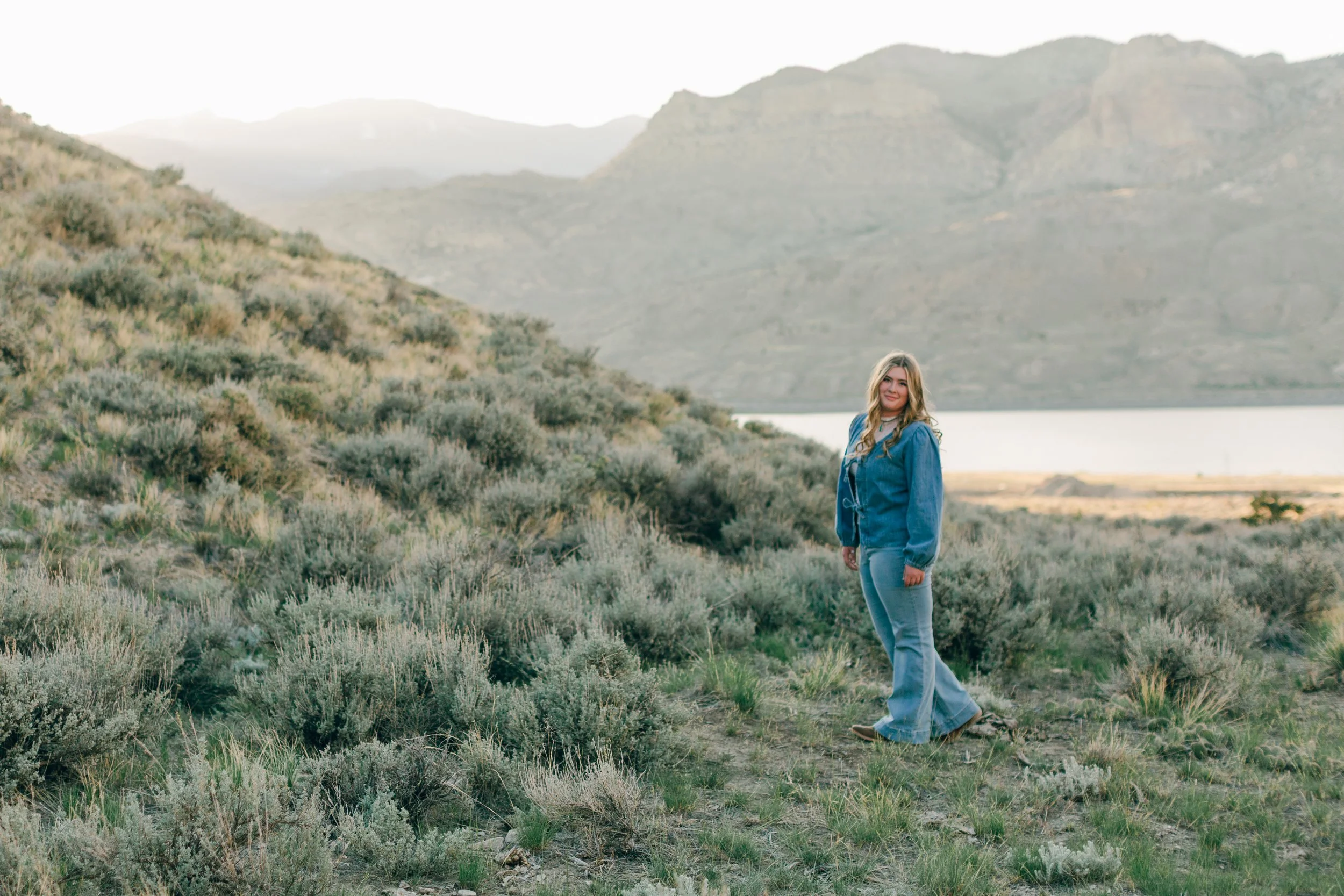 Senior portrait in Wyoming sagebrush on Sheep Mountain Trail with Rattlesnake Mountain looming in the background outside Cody at sunset.