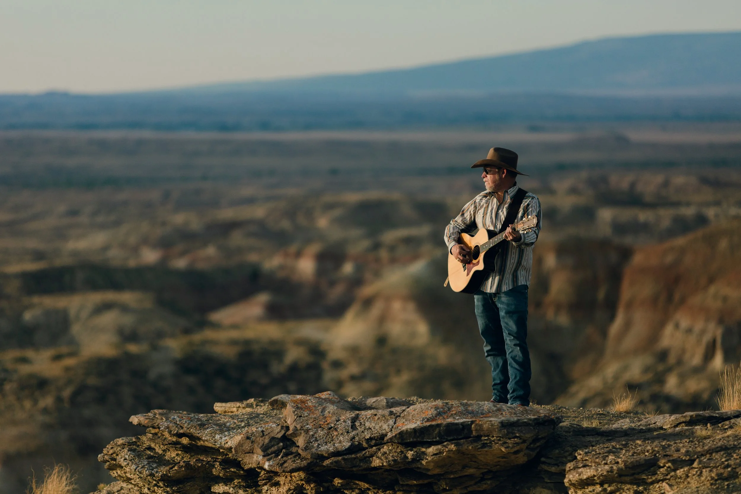 Aaron Walker playing acoustic guitar on a rocky ledge in the Badlands near Cody, Wyoming.