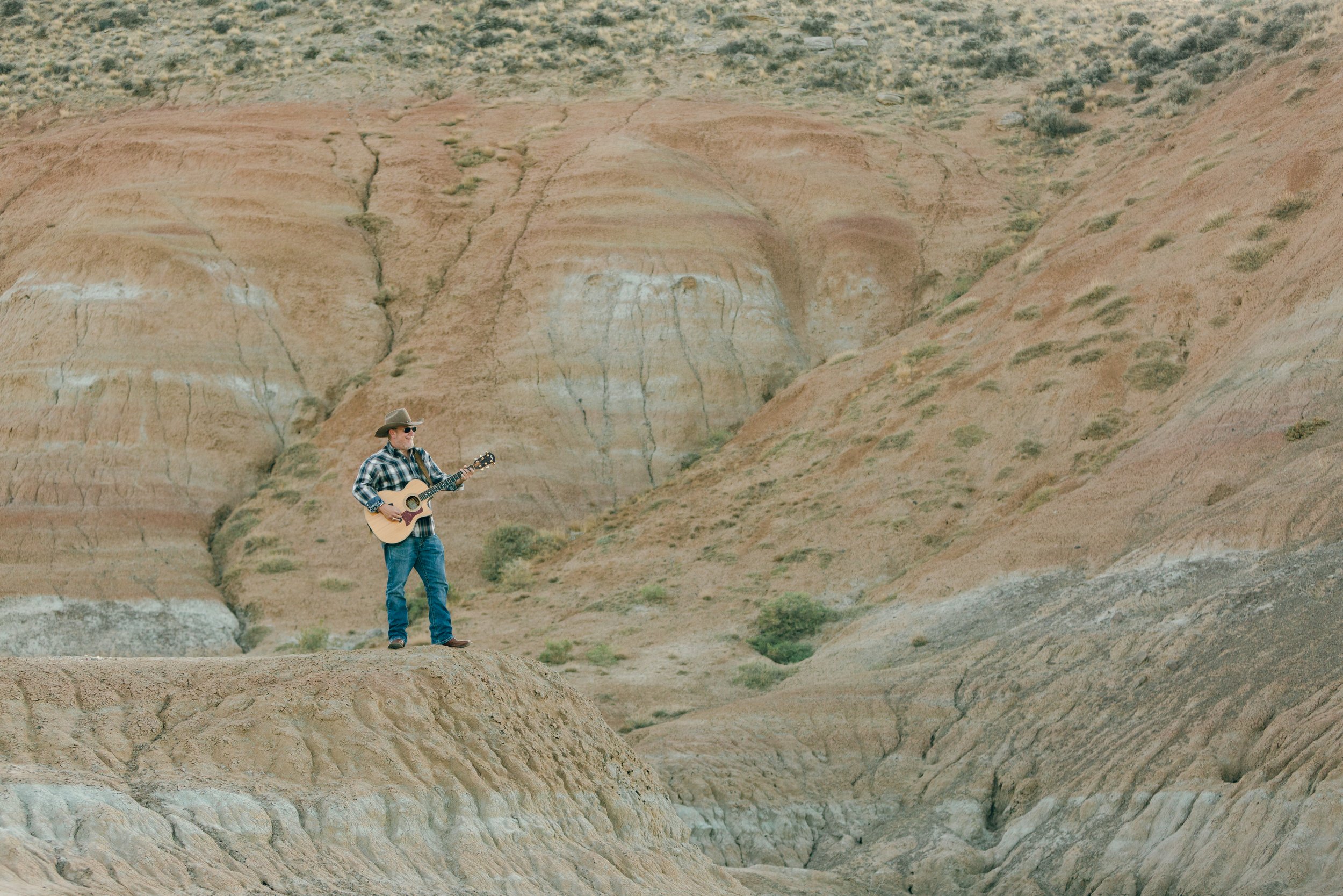 Wyoming musician Aaron Walker playing acoustic guitar among the colorful Badlands formations near Cody, Wyoming.