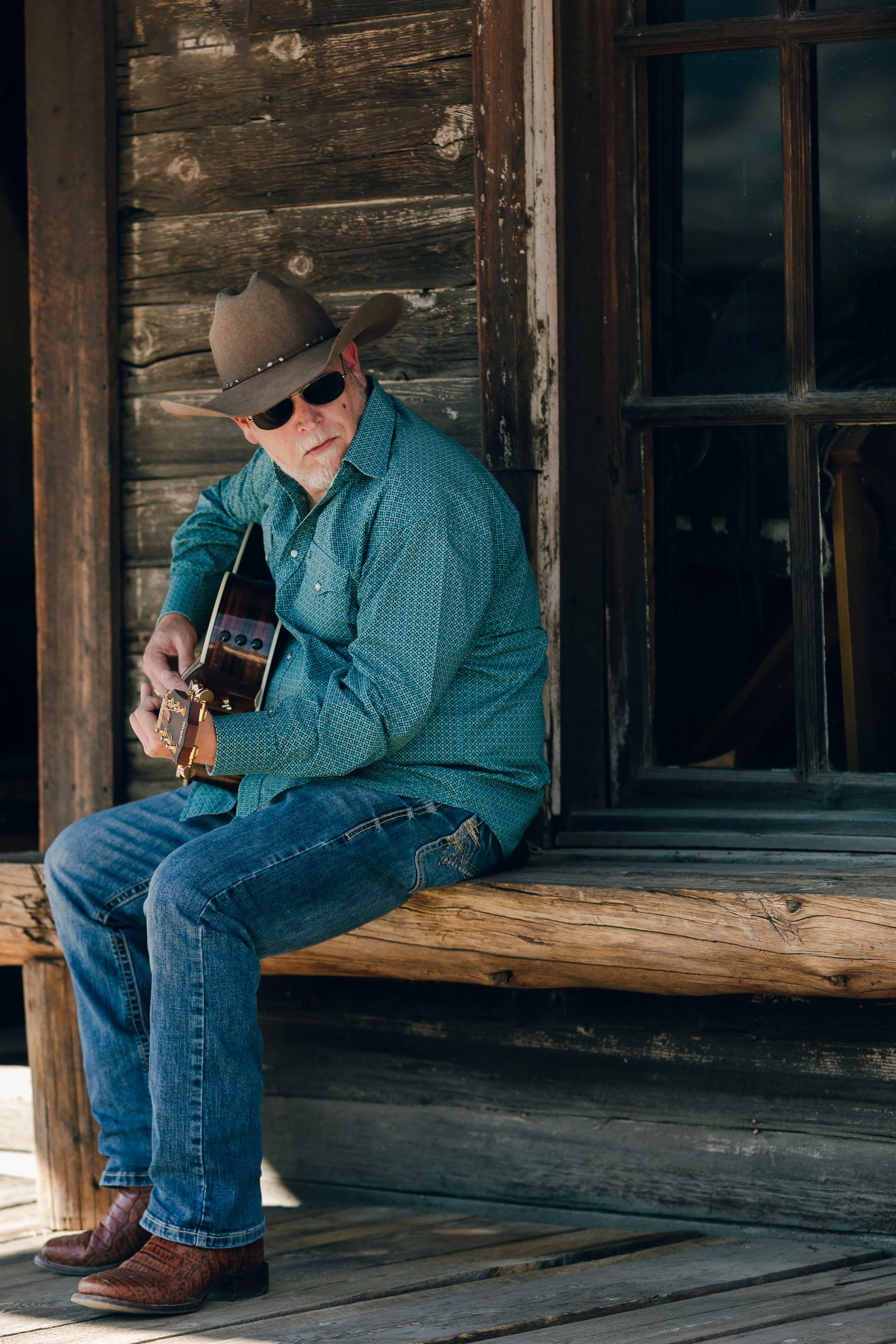 Portrait of Wyoming musician Aaron Walker playing guitar on the porch of a historic building at Old Trail Town in Cody, Wyoming.
