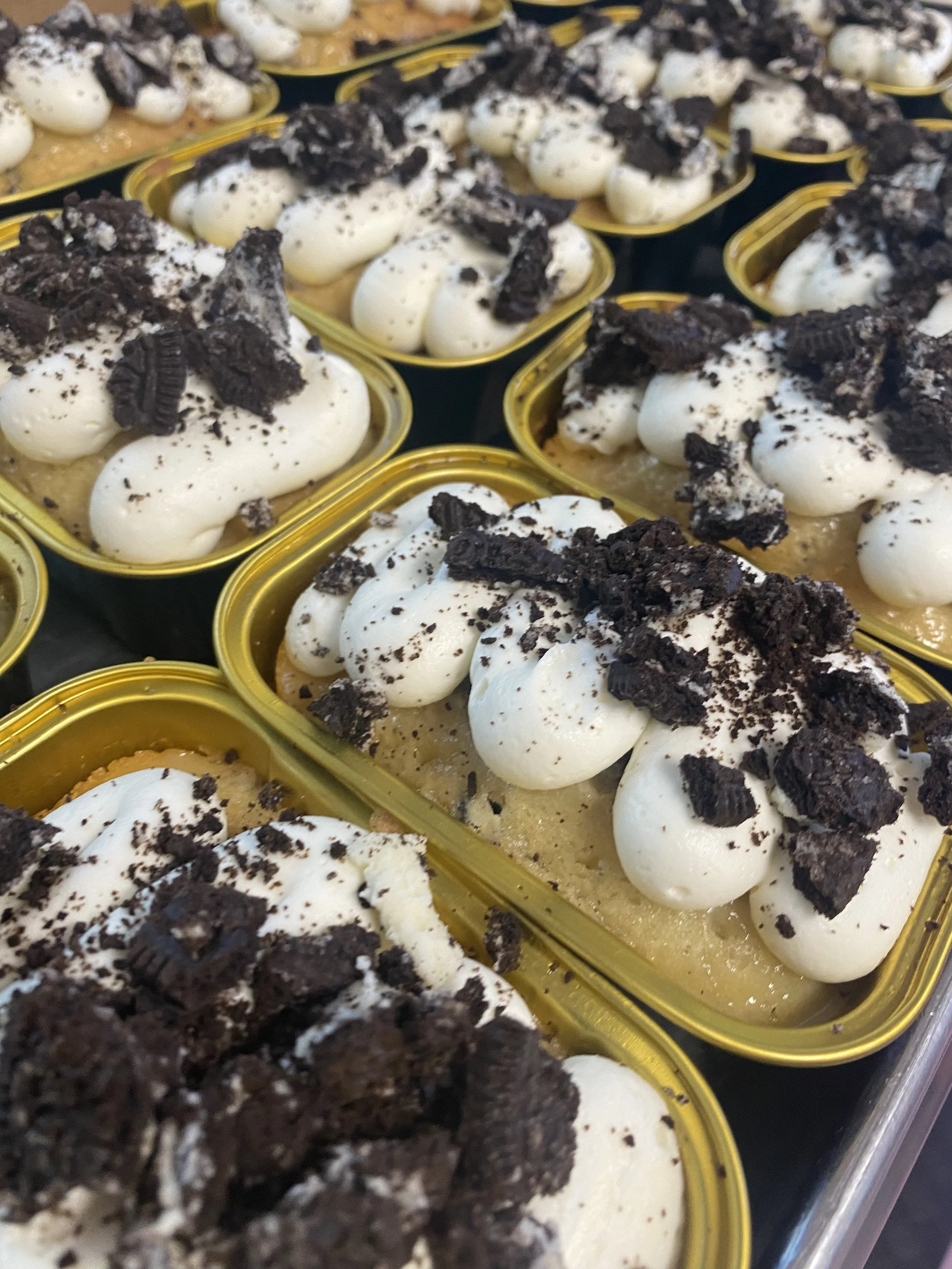 Multiple servings of Oreo ice cream topped with whipped cream and crushed Oreo cookies in small rectangular containers with gold rims.