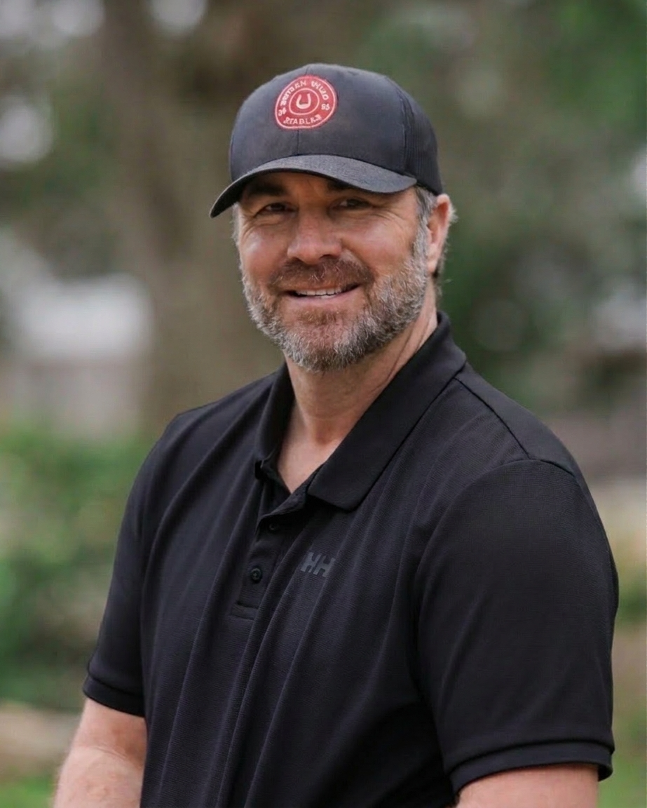 A smiling man with a beard wearing a black cap and a dark grey polo shirt outdoors.