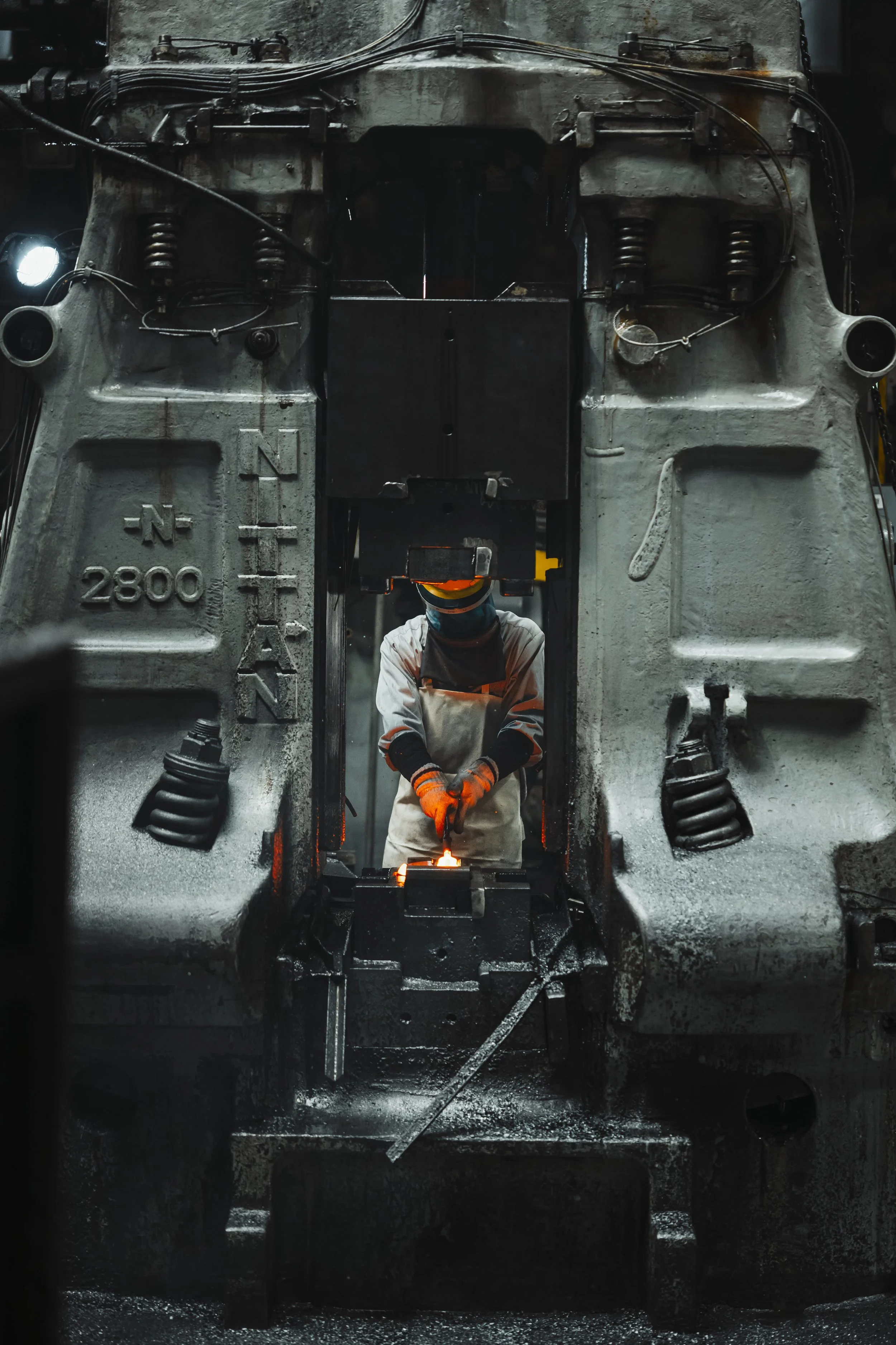 A worker in protective gear, including gloves and a face shield, welding inside a large industrial metal structure in a factory or manufacturing setting.
