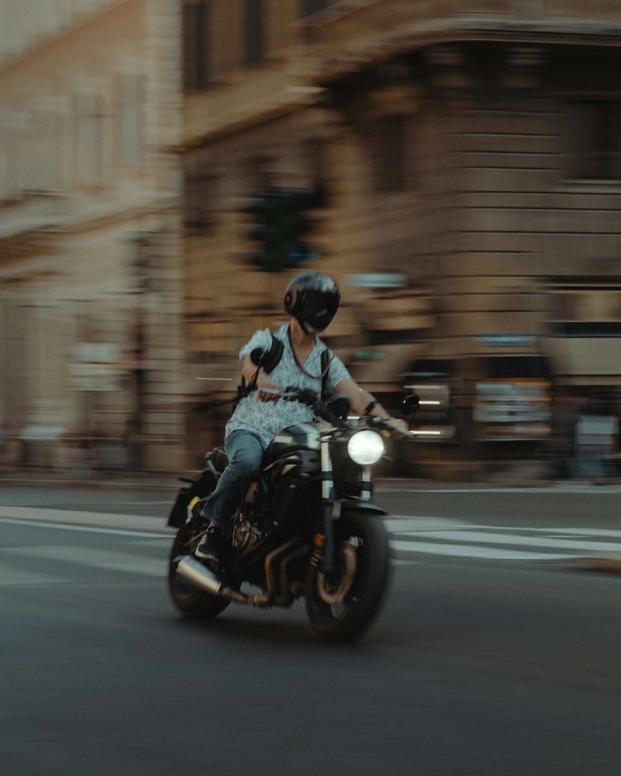 Person riding a motorcycle on city street, wearing a helmet and casual clothing.