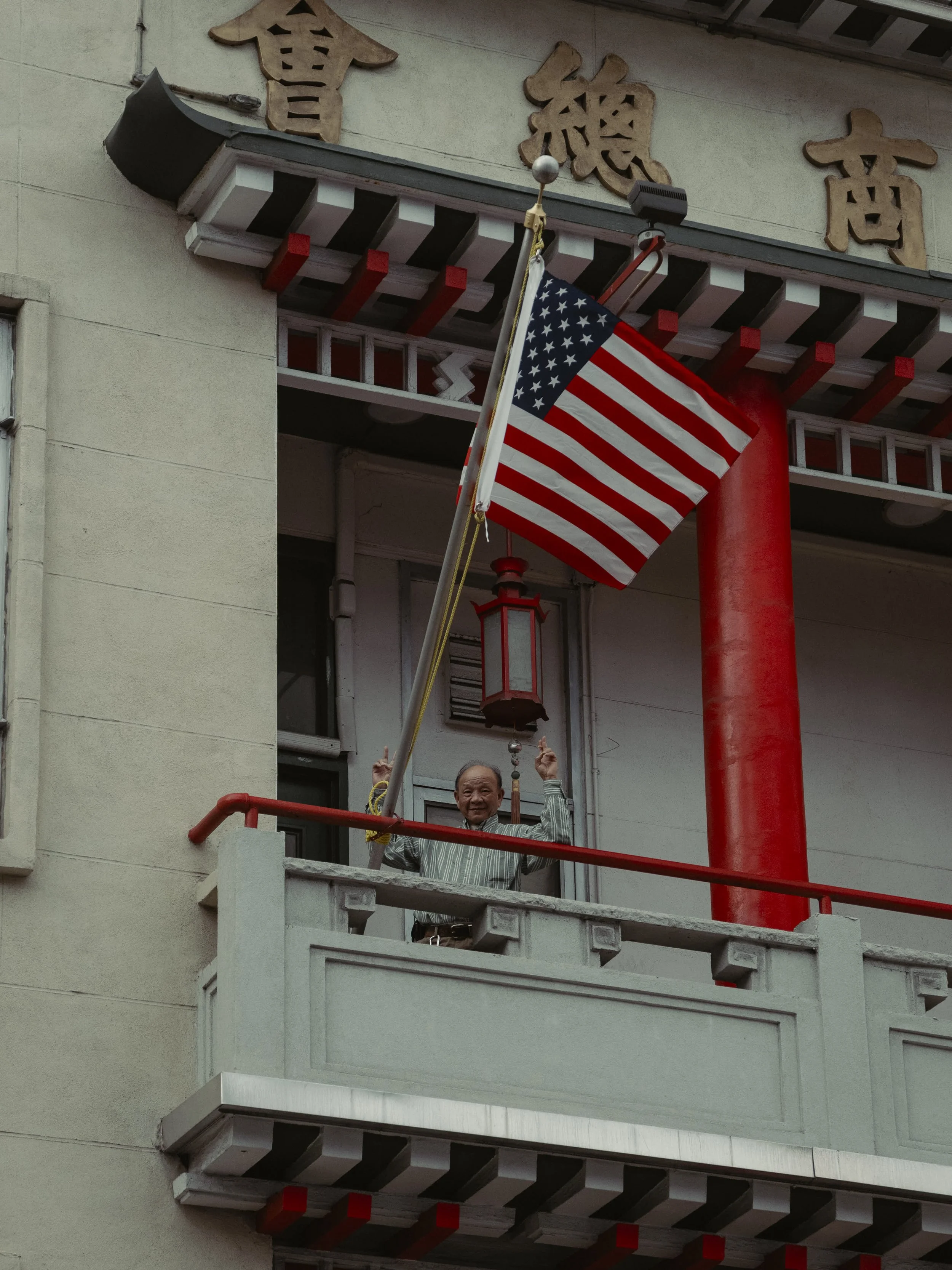 A man standing on a balcony of a building with Chinese architectural elements, waving an American flag.