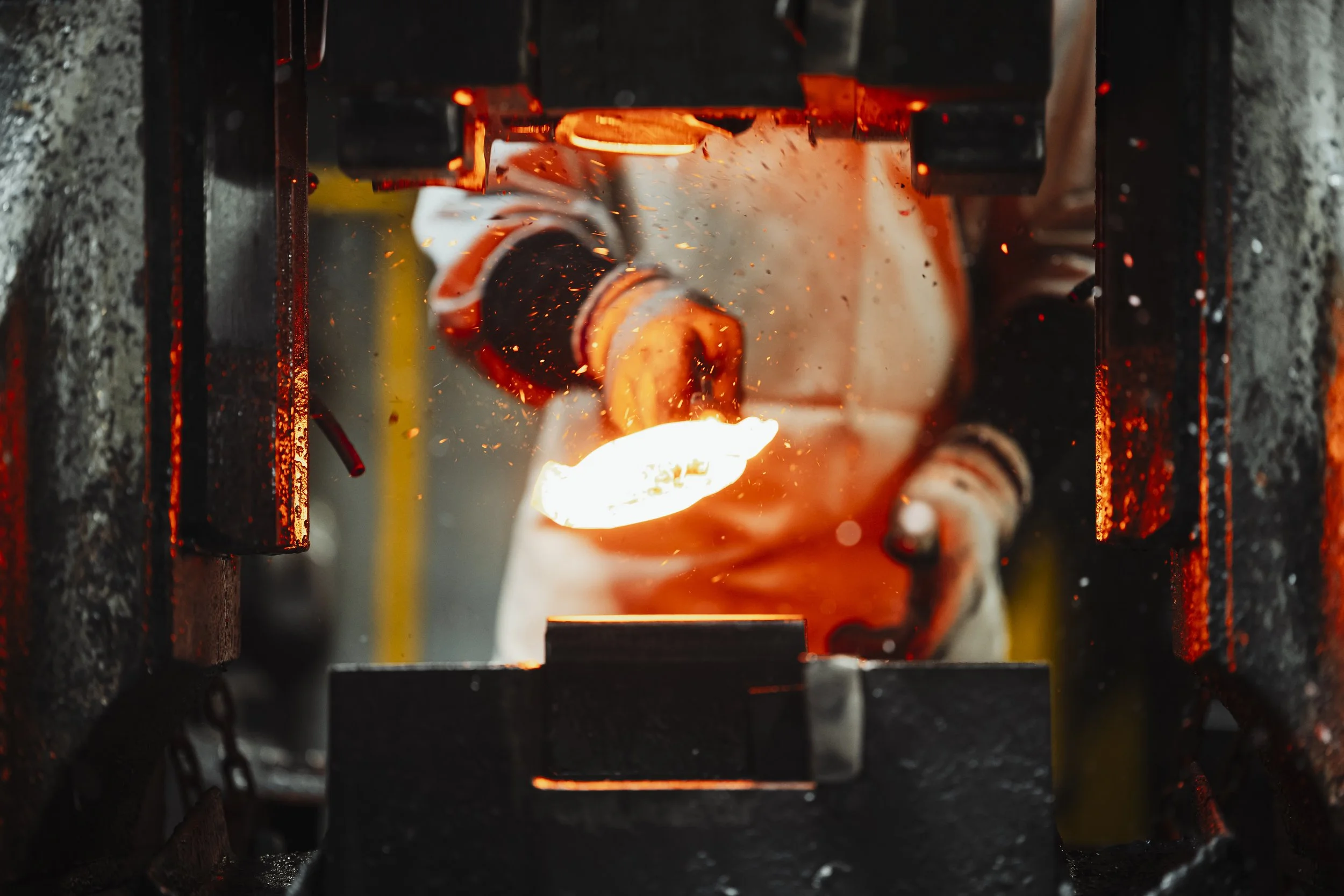 A glassblower shaping molten glass in a furnace.