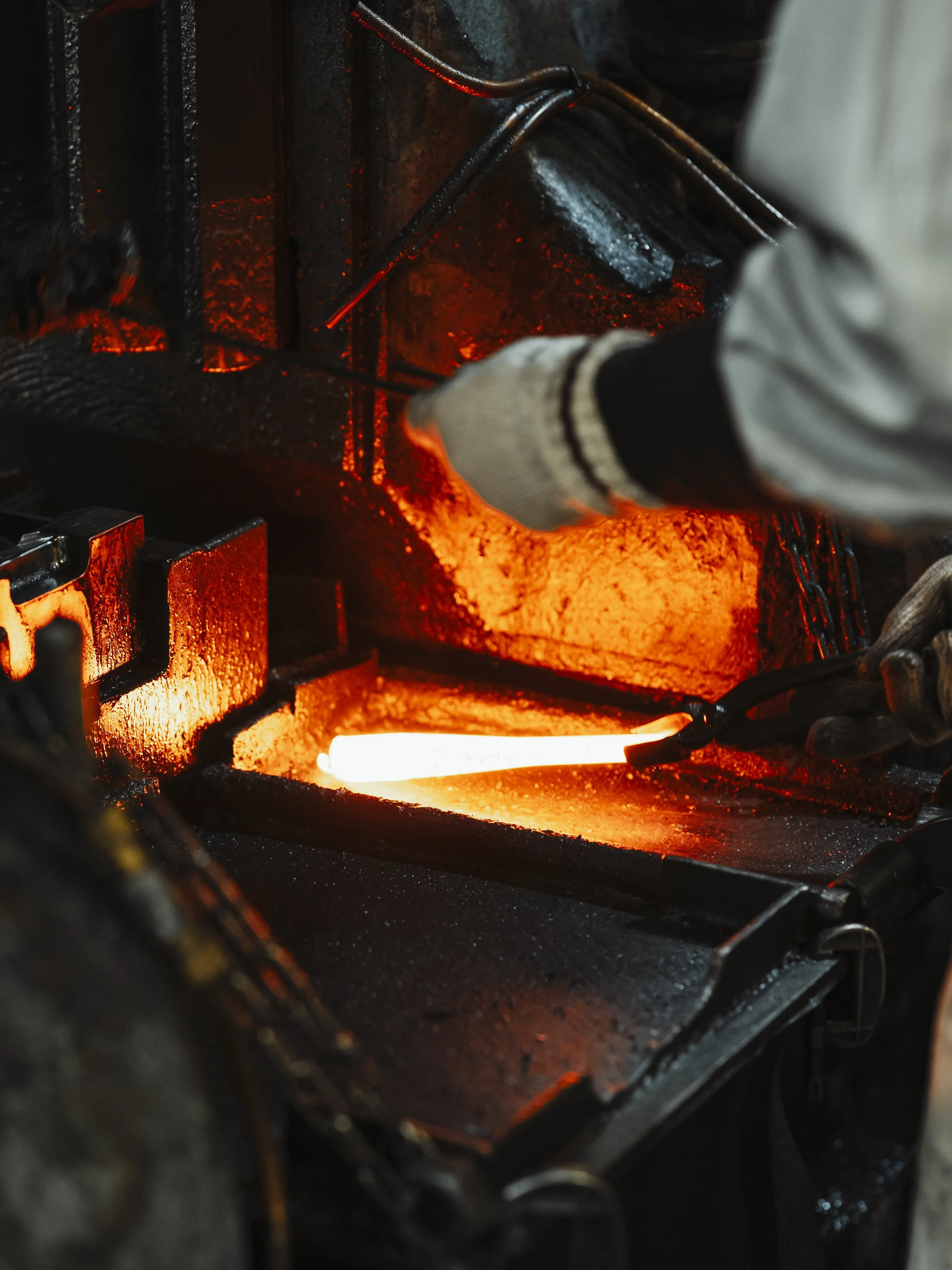 A blacksmith working with glowing hot metal on an anvil, using tongs to shape the molten material in a forge.