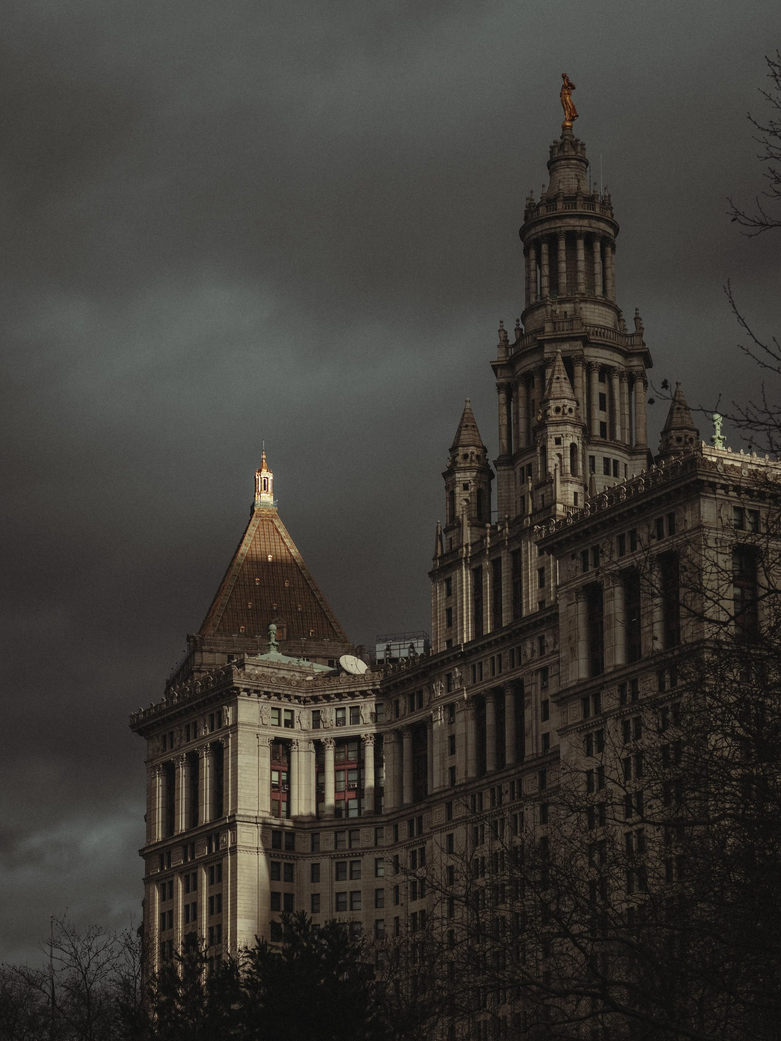 A historic skyscraper with ornate architecture, topped with a Statue of Liberty replica, set against a dark cloudy sky.