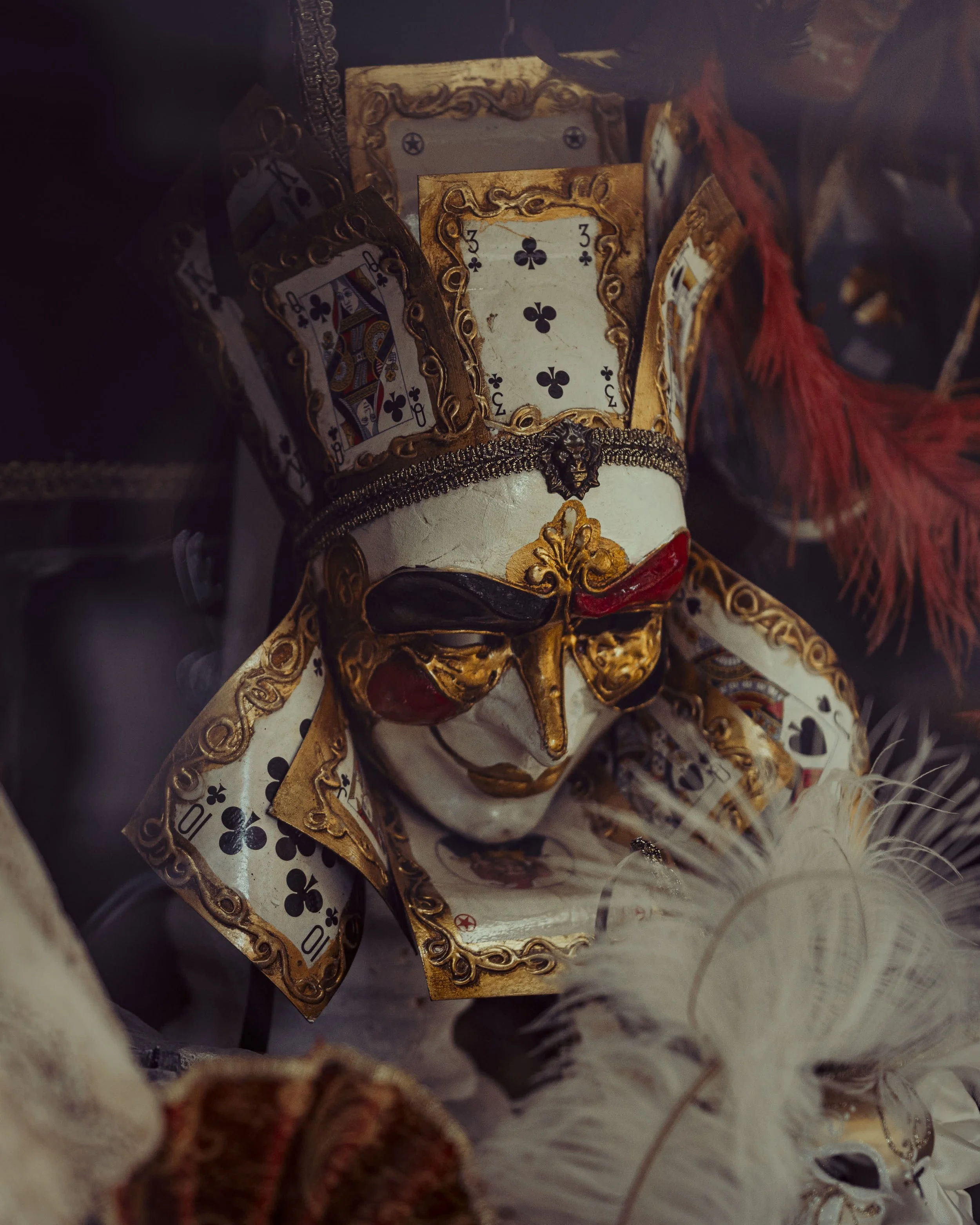 A decorative mask with gold, black, and red accents, adorned with playing cards and ornate designs.
