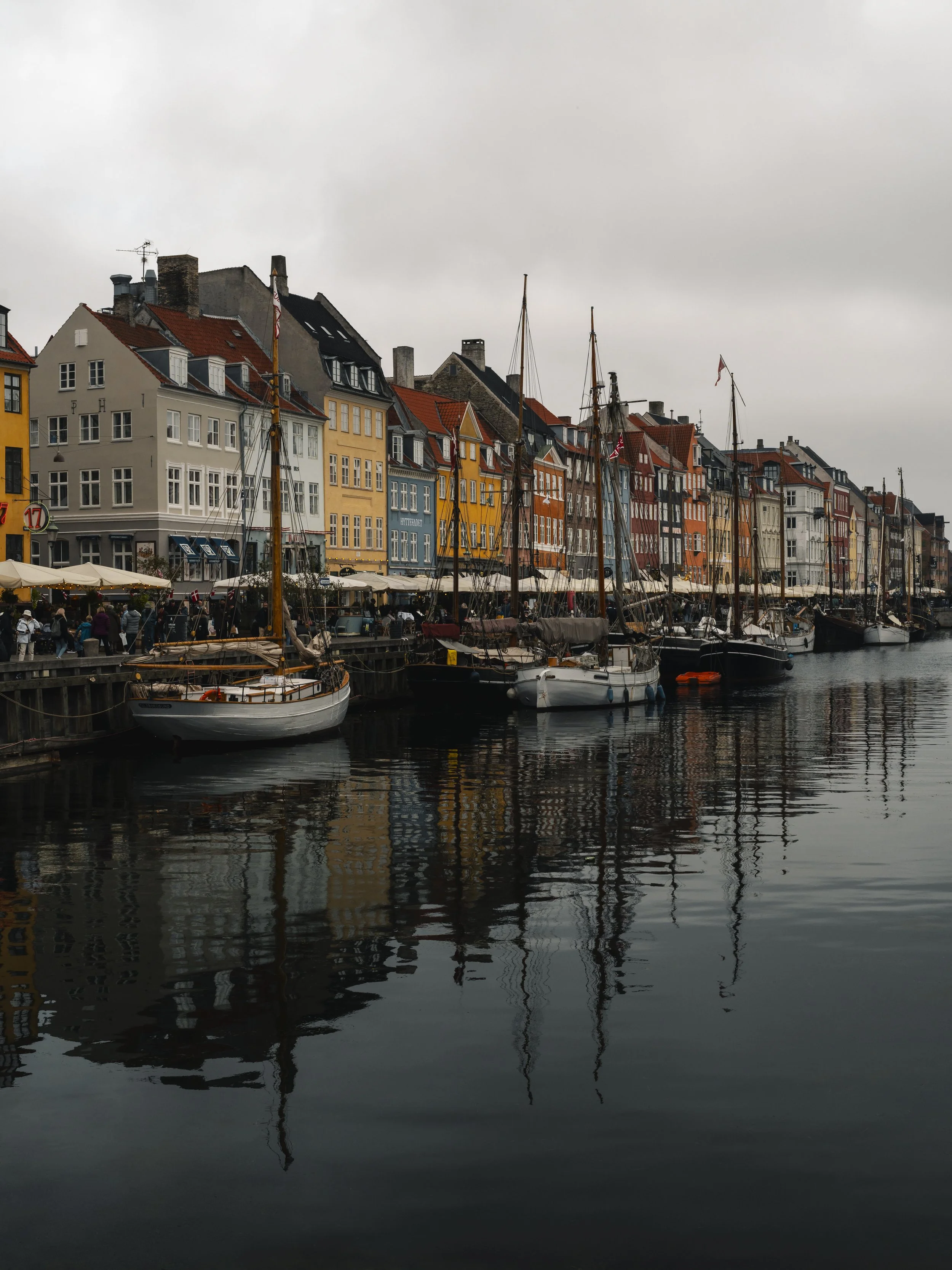 Colorful buildings line a waterfront with sailboats docked along the pier, and their reflections visible in the water.