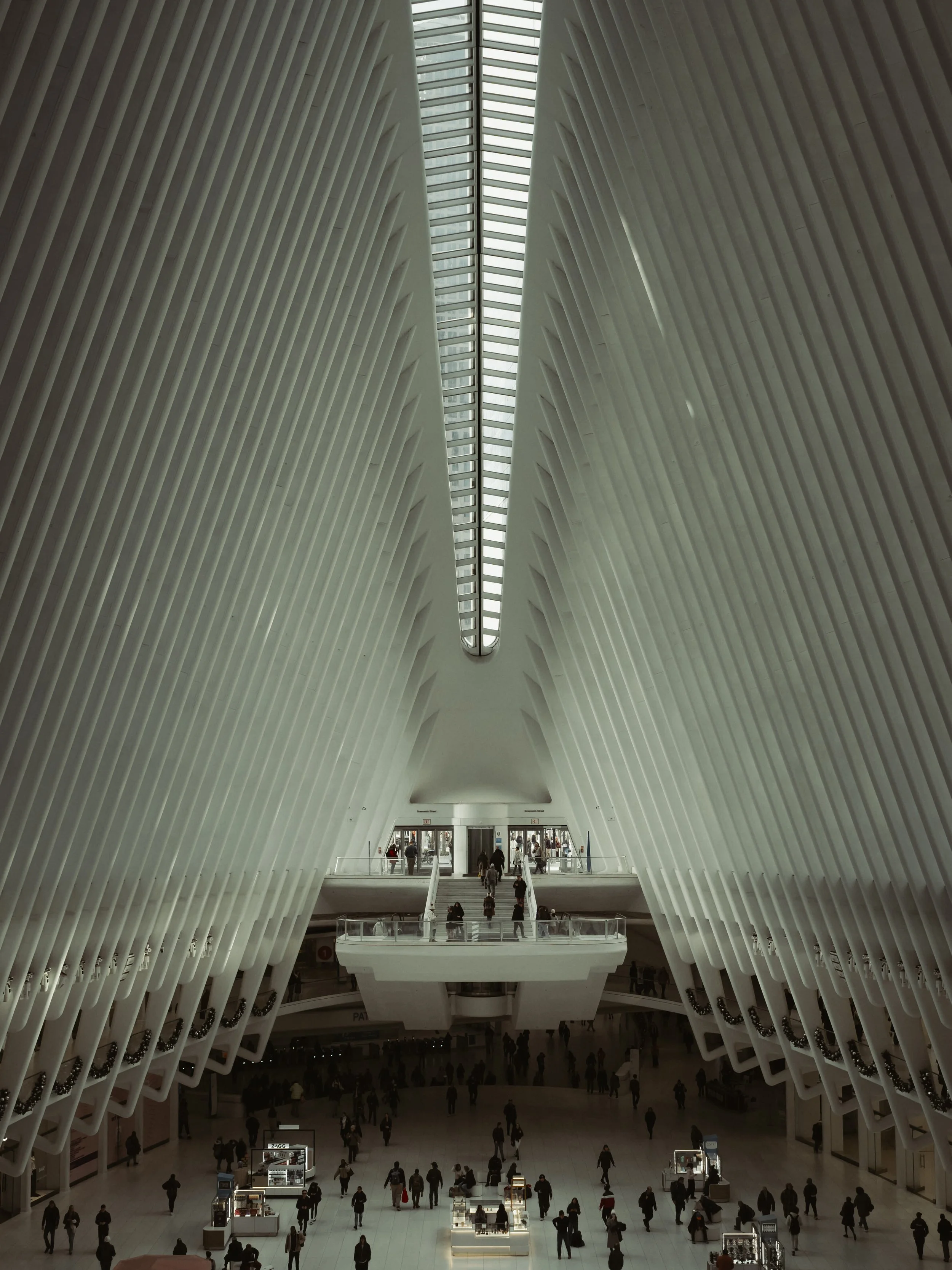 Interior view of the Oculus transportation hub with white architectural design and large skylight, people walking inside.