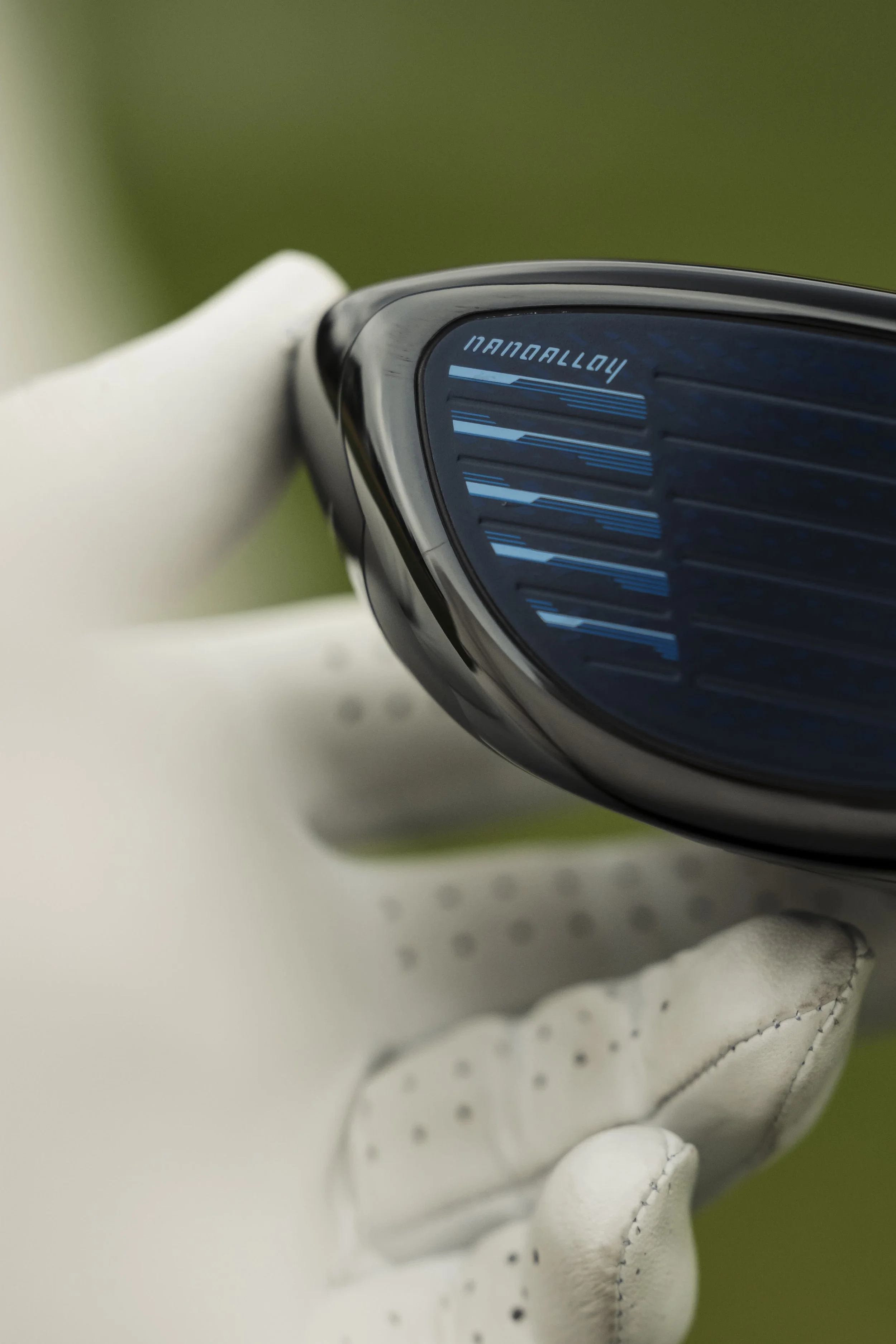 Close-up of a golf club head with a blue face and white golf glove.