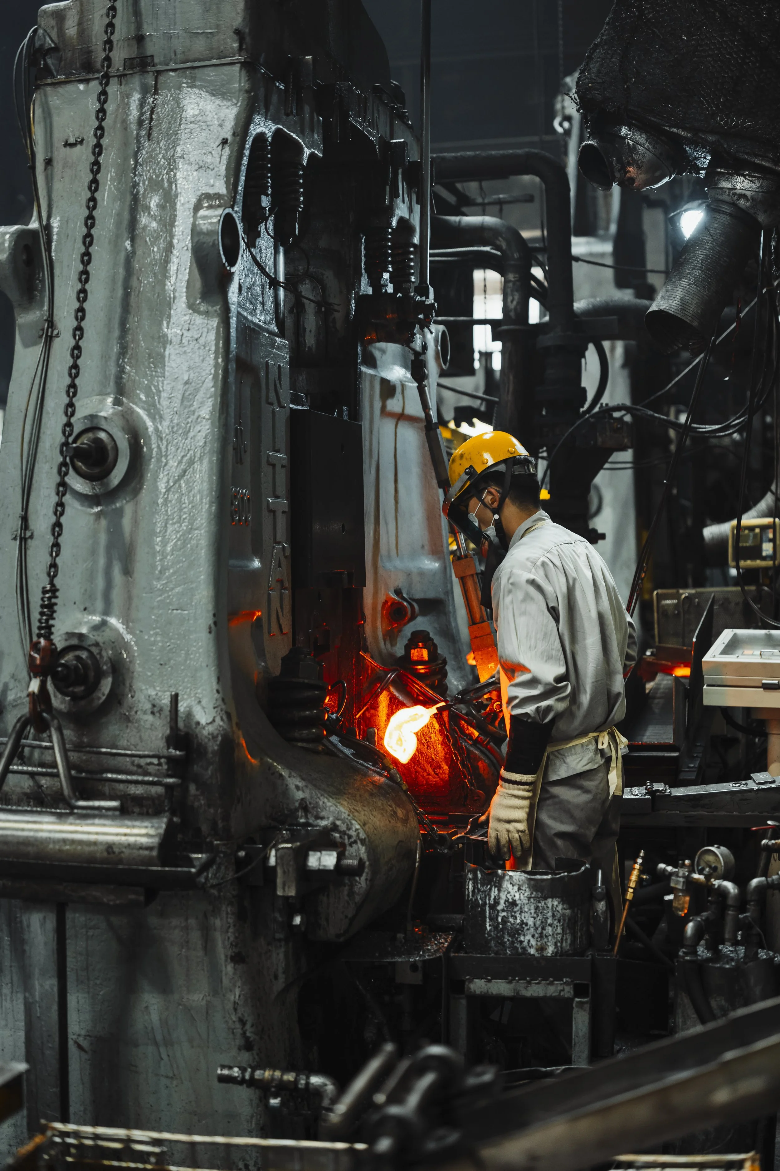 A worker in safety gear, including a yellow helmet and gloves, is welding a large piece of industrial machinery in a factory.