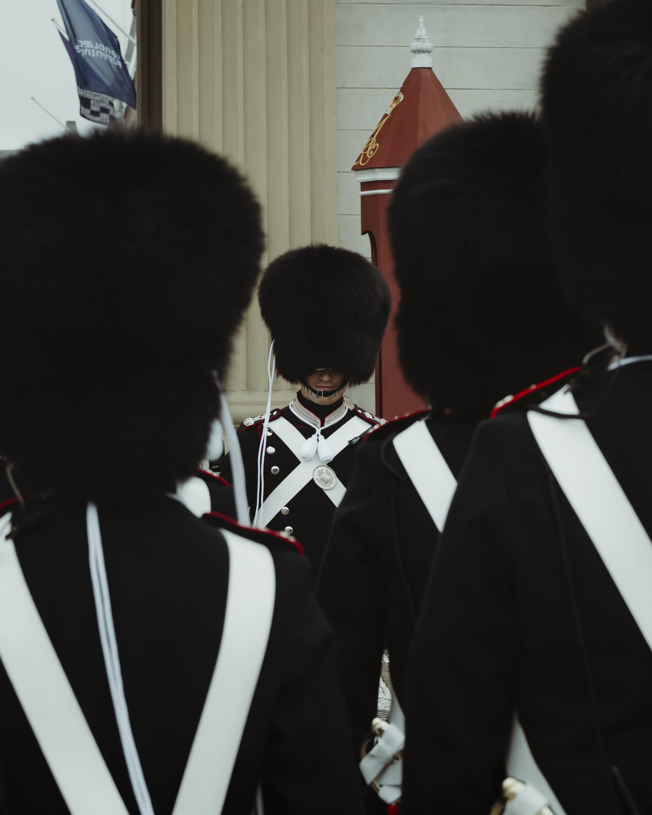 A group of uniformed guards wearing bearskin hats, with one guard in the center checking a device, as seen during a ceremonial event.
