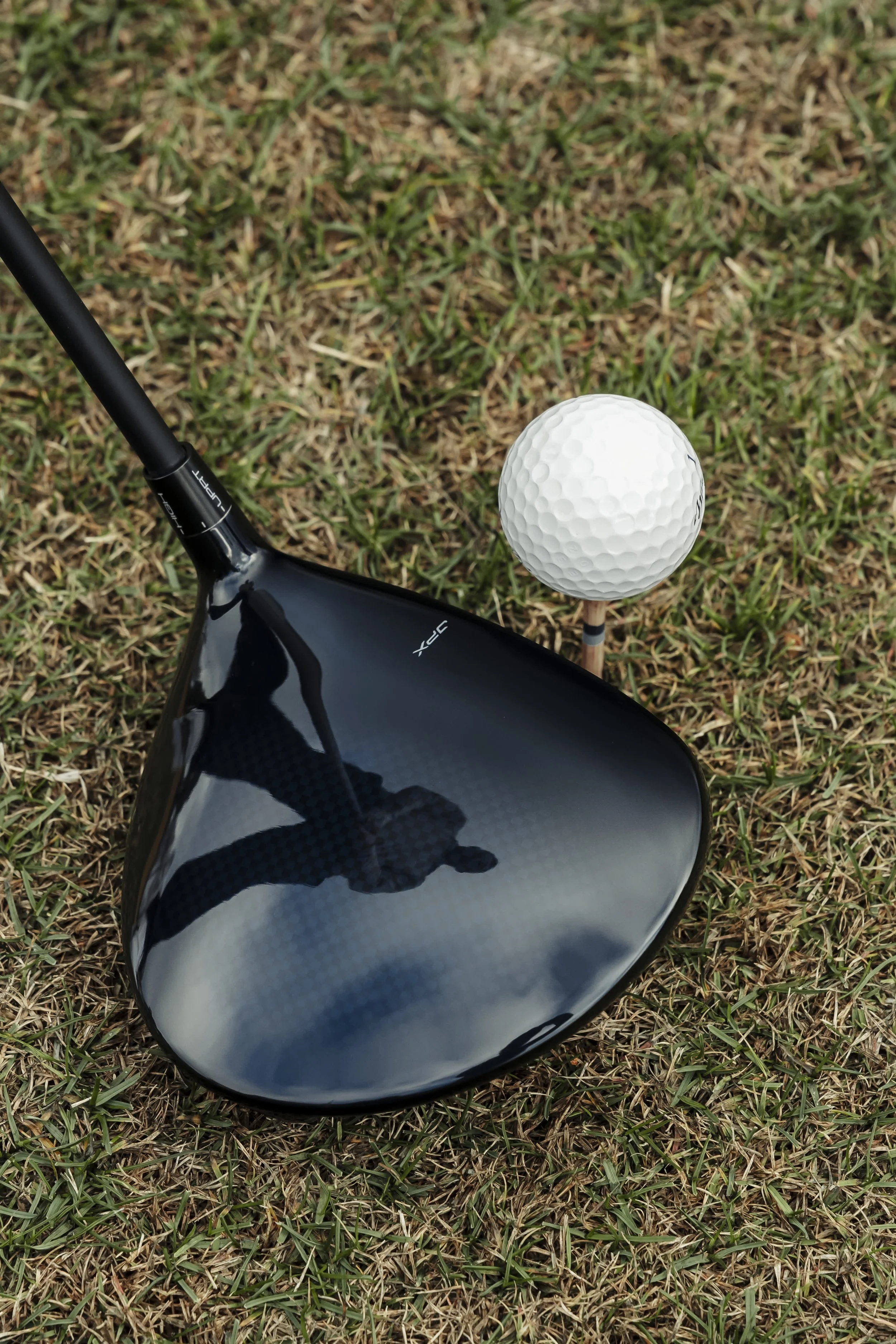 A golf club and a golf ball on a tee on grass.