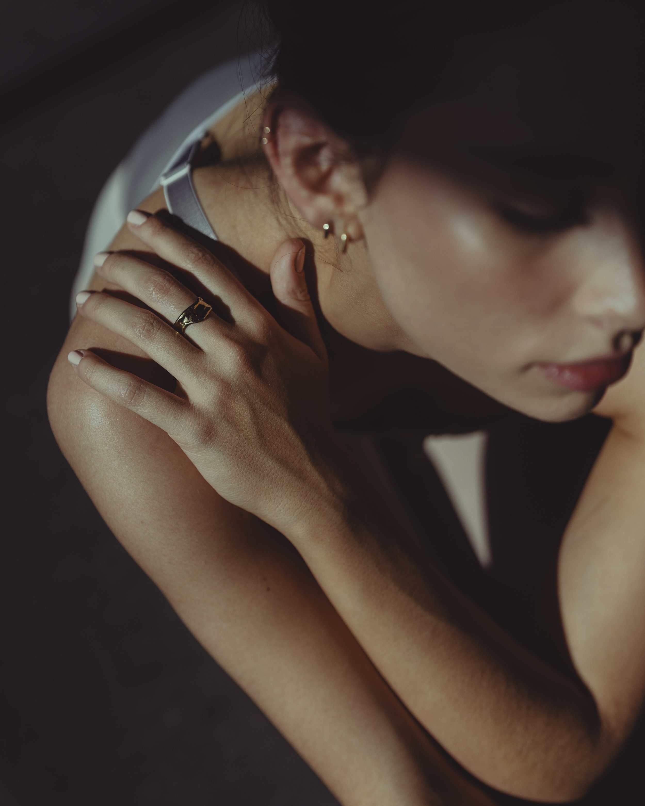 A woman with dark hair and earrings, resting her arm on her shoulder, in a contemplative pose.
