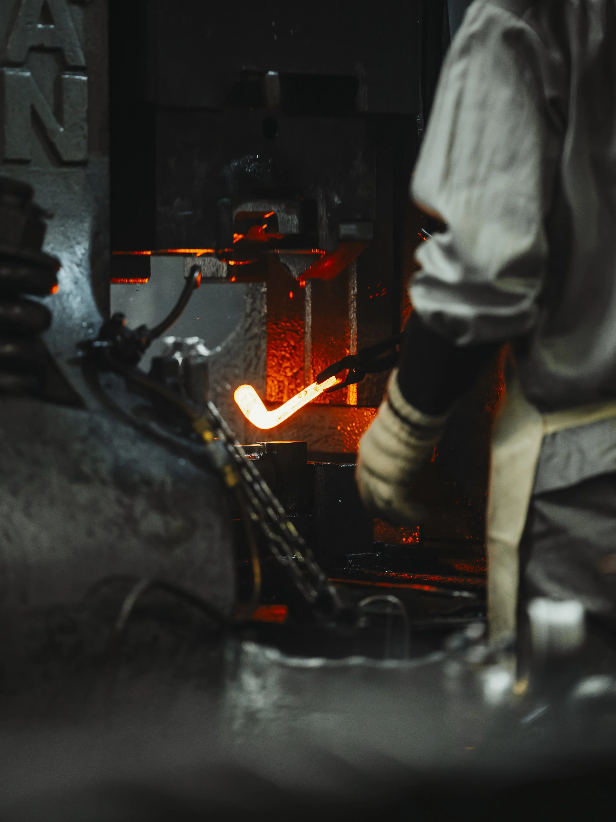 A worker is forging or shaping a glowing hot metal piece using a hydraulic press in an industrial setting.