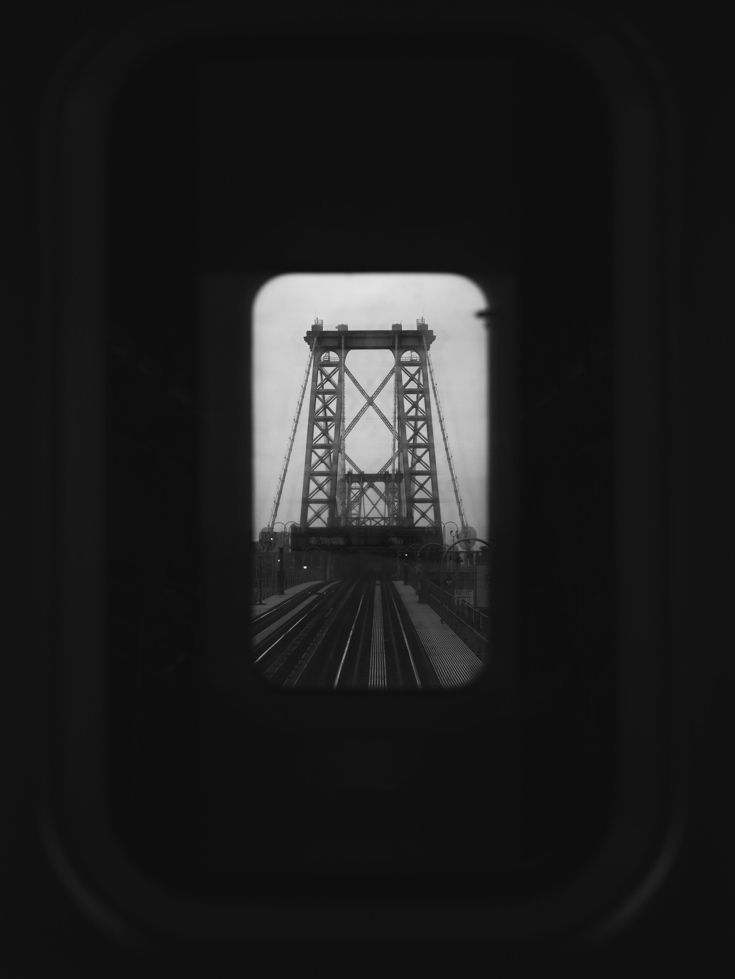 View of a bridge tower through an oval window with train tracks leading towards it in black and white.