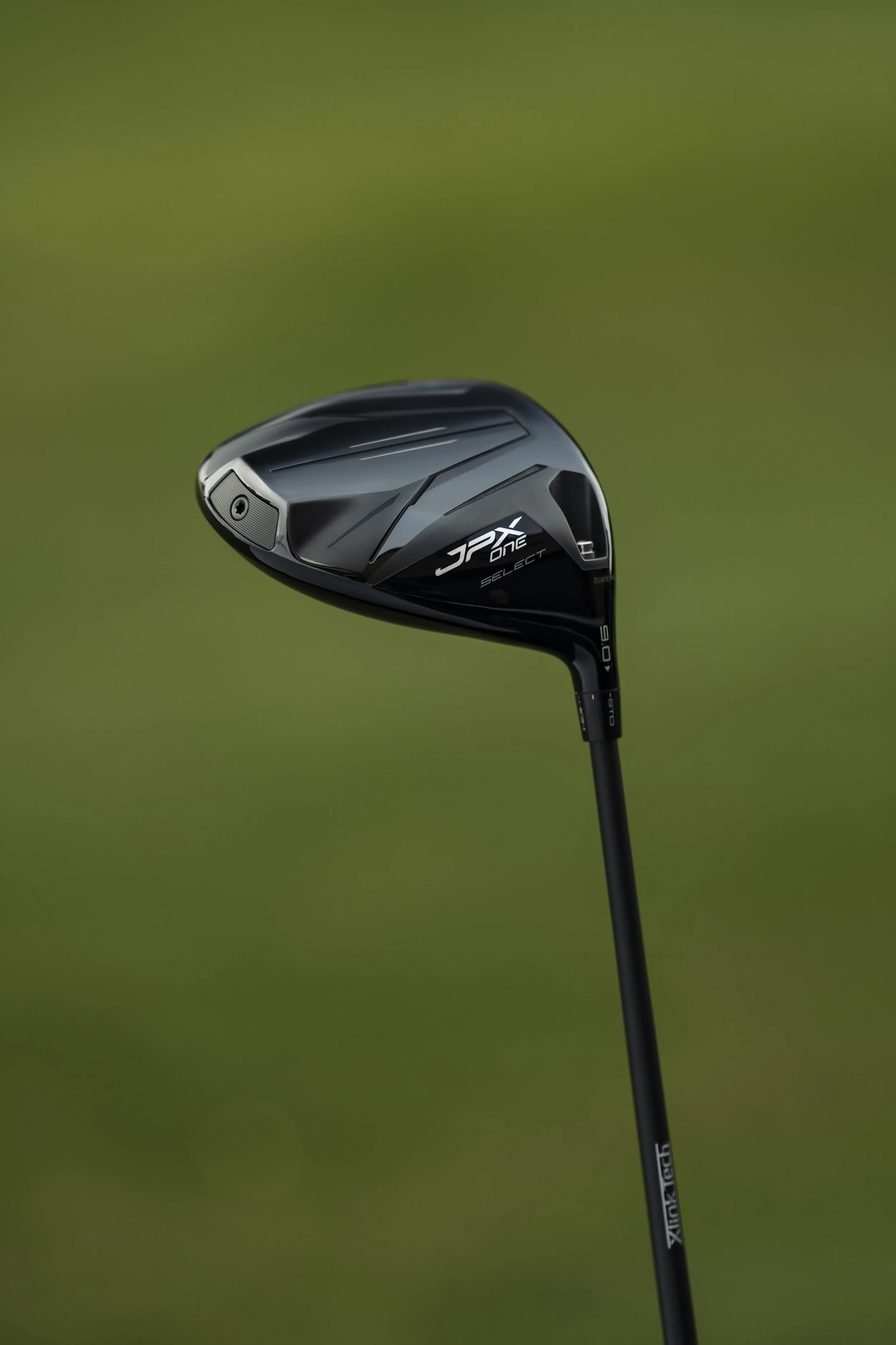 Close-up of a black golf club driver against a green background.