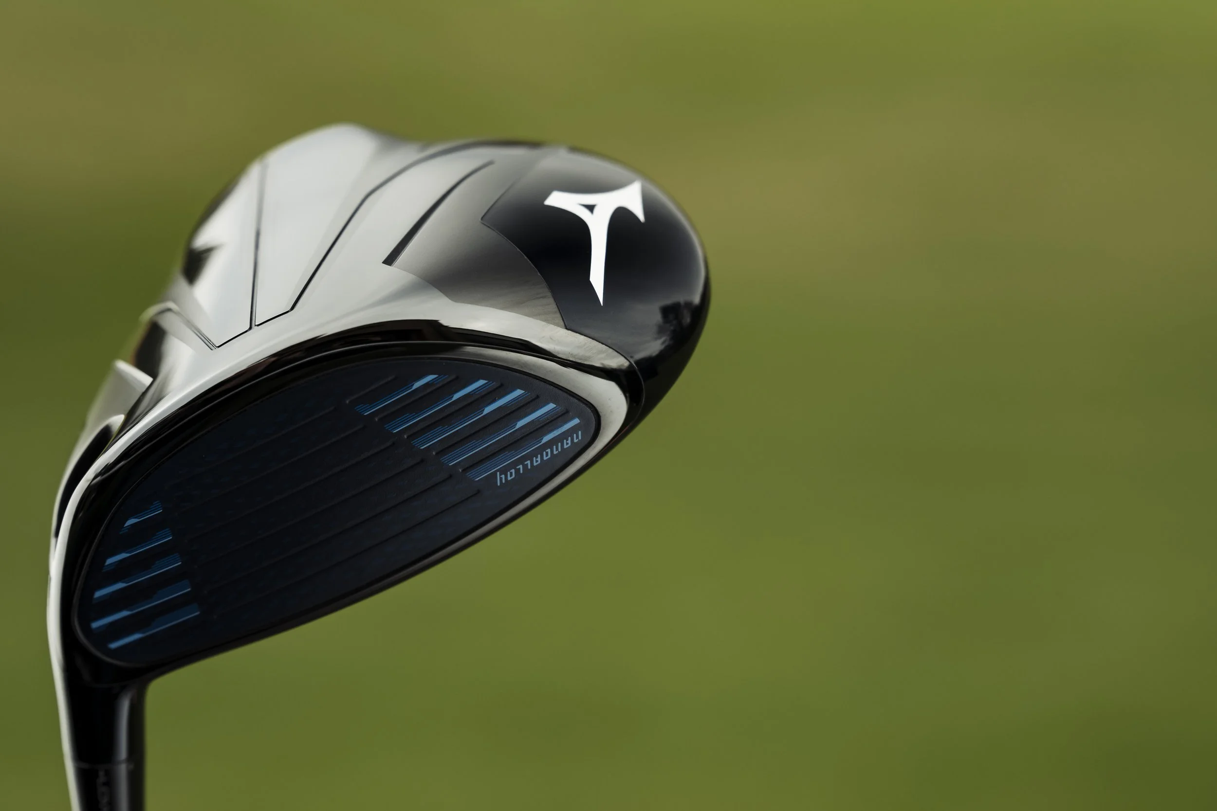 Close-up of a Callaway golf club with a black and silver head and blue grooves on the face, set against a blurred green background.