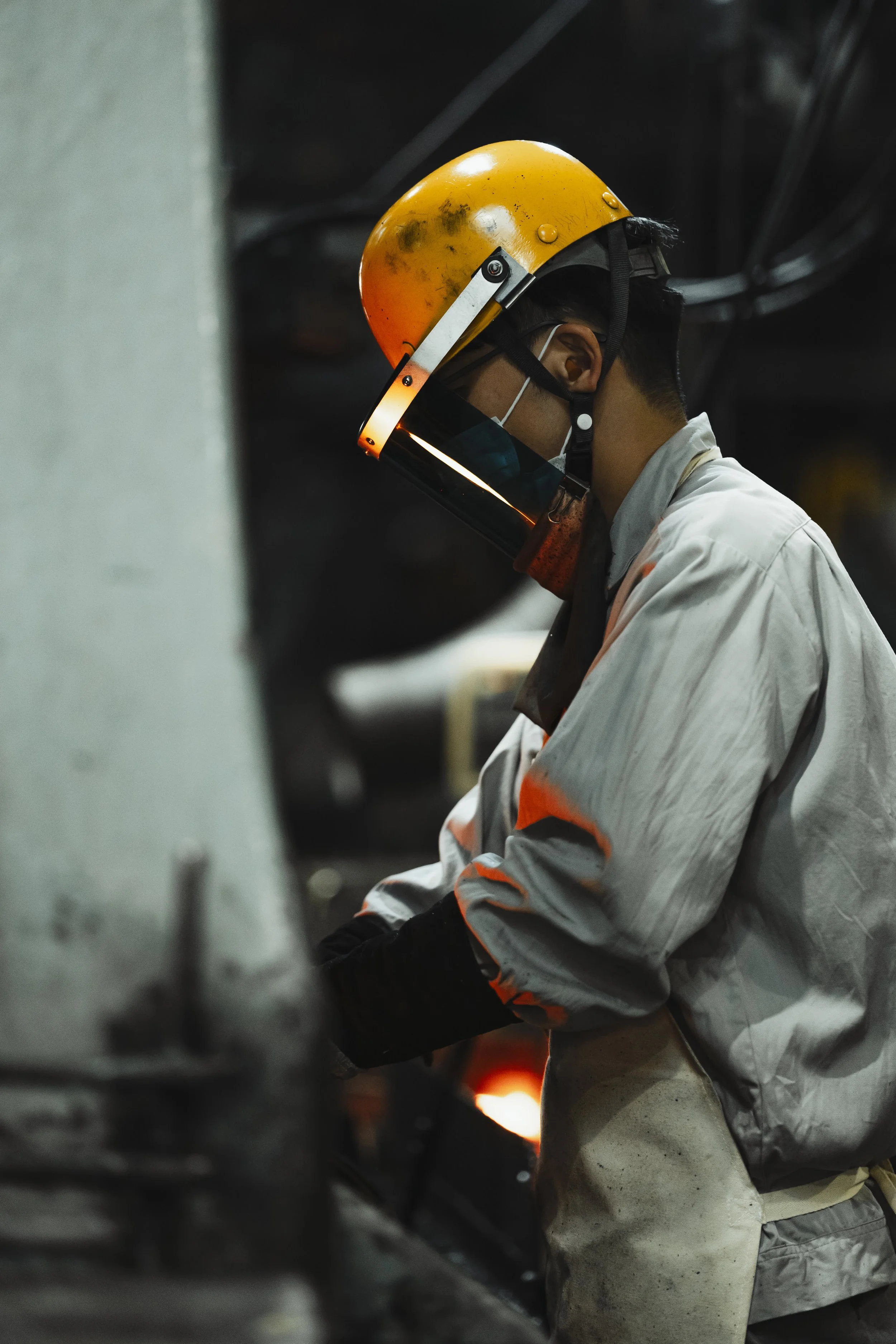 A worker wearing a yellow safety helmet, face mask, and protective white clothing working in an industrial setting.