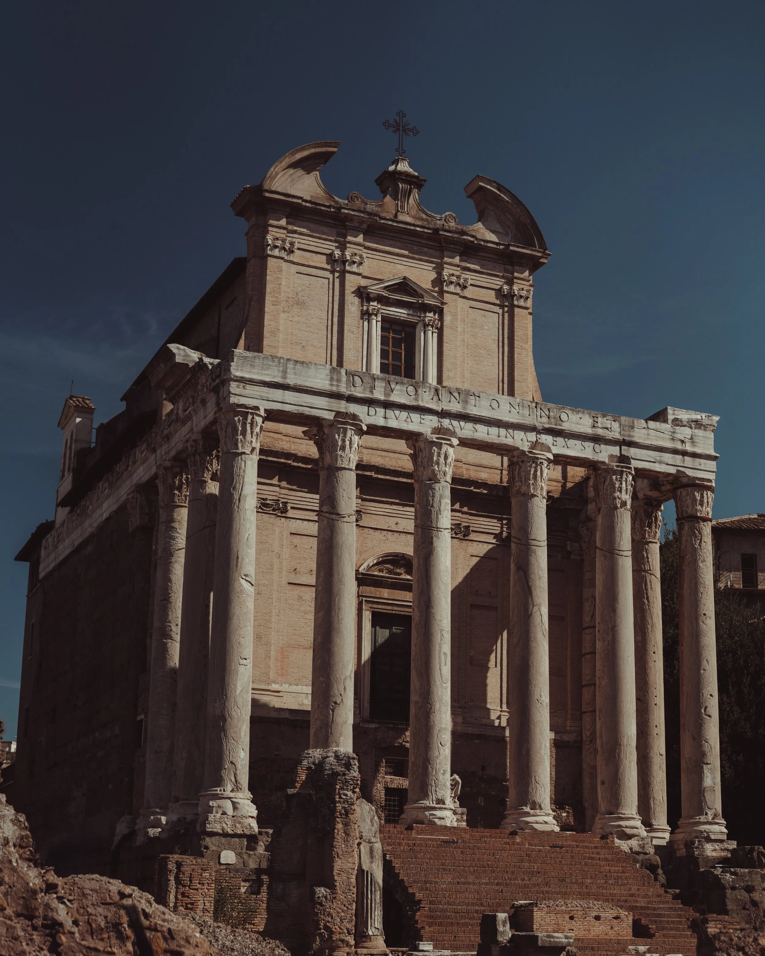 Ancient Roman ruins with tall columns and steps leading up to a brick building with a cross on top.