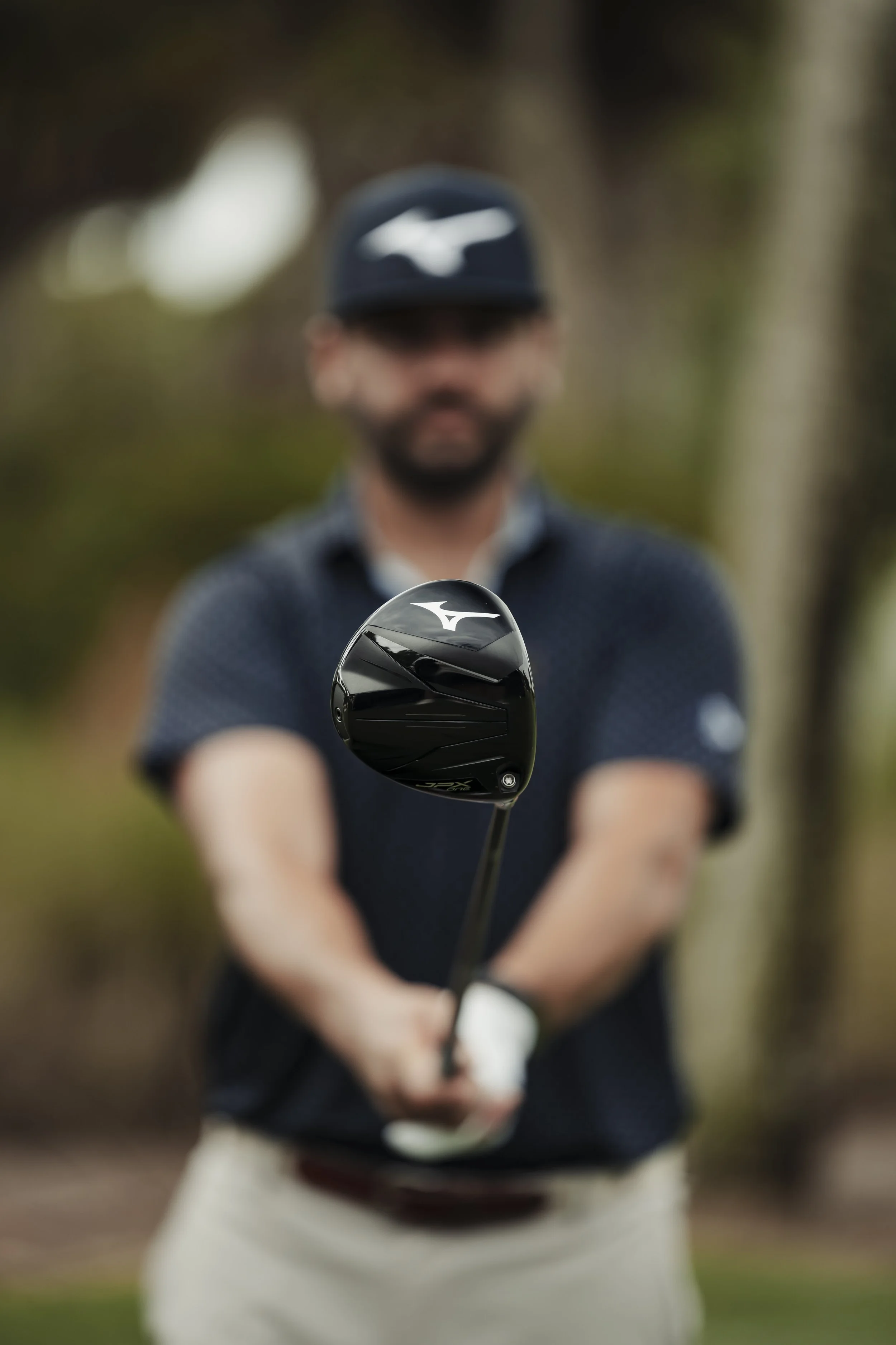 A man holding a golf club on a golf course, with a blurred background of trees.