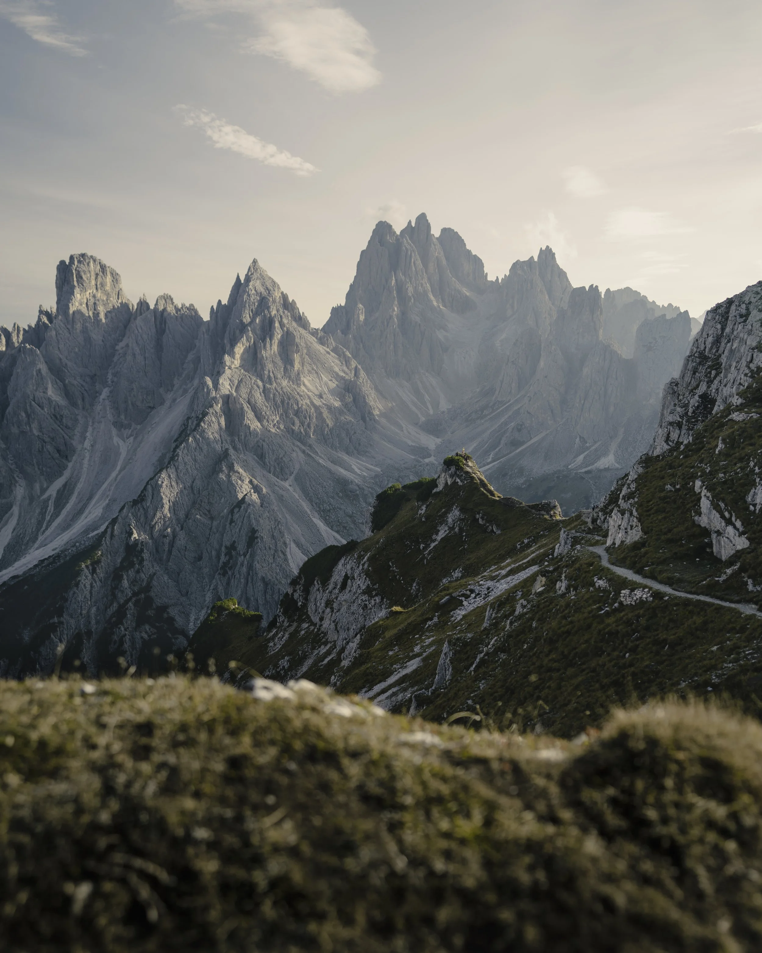 Mountain landscape with rocky peaks, green slopes, and a cloudy sky.