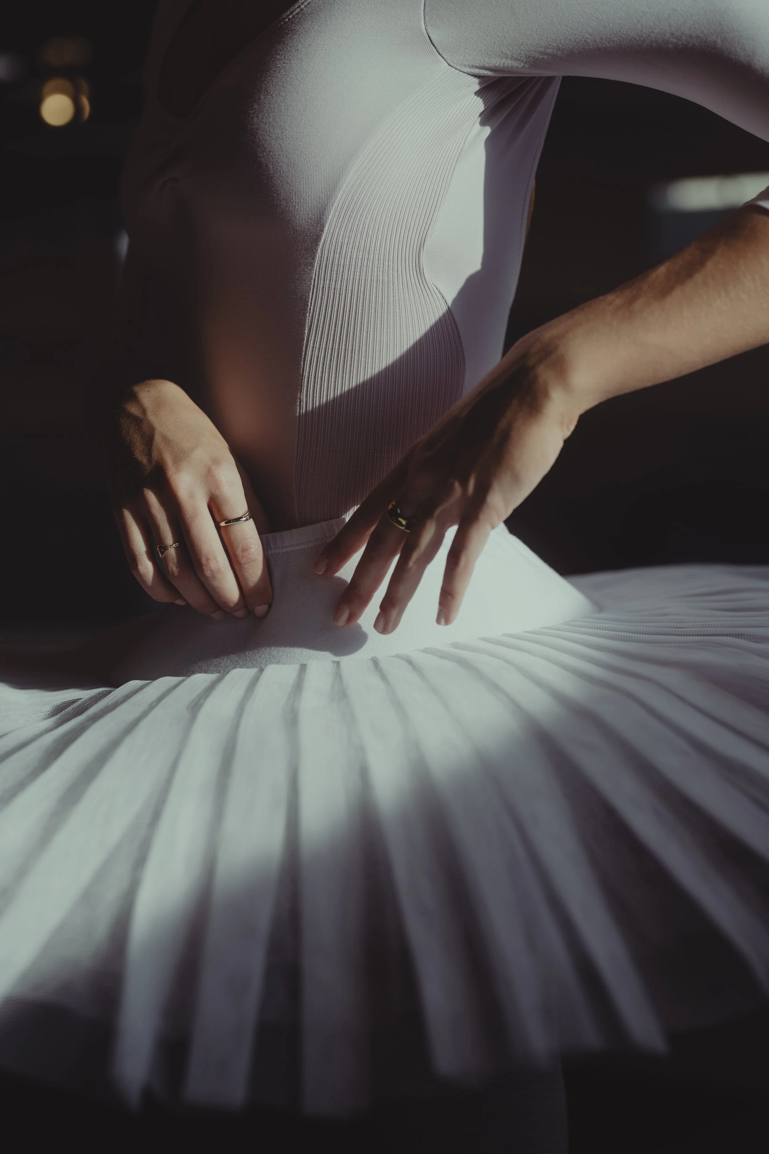 Close-up of a person wearing a white top and multiple rings, turning pages in a large open book in dim lighting.