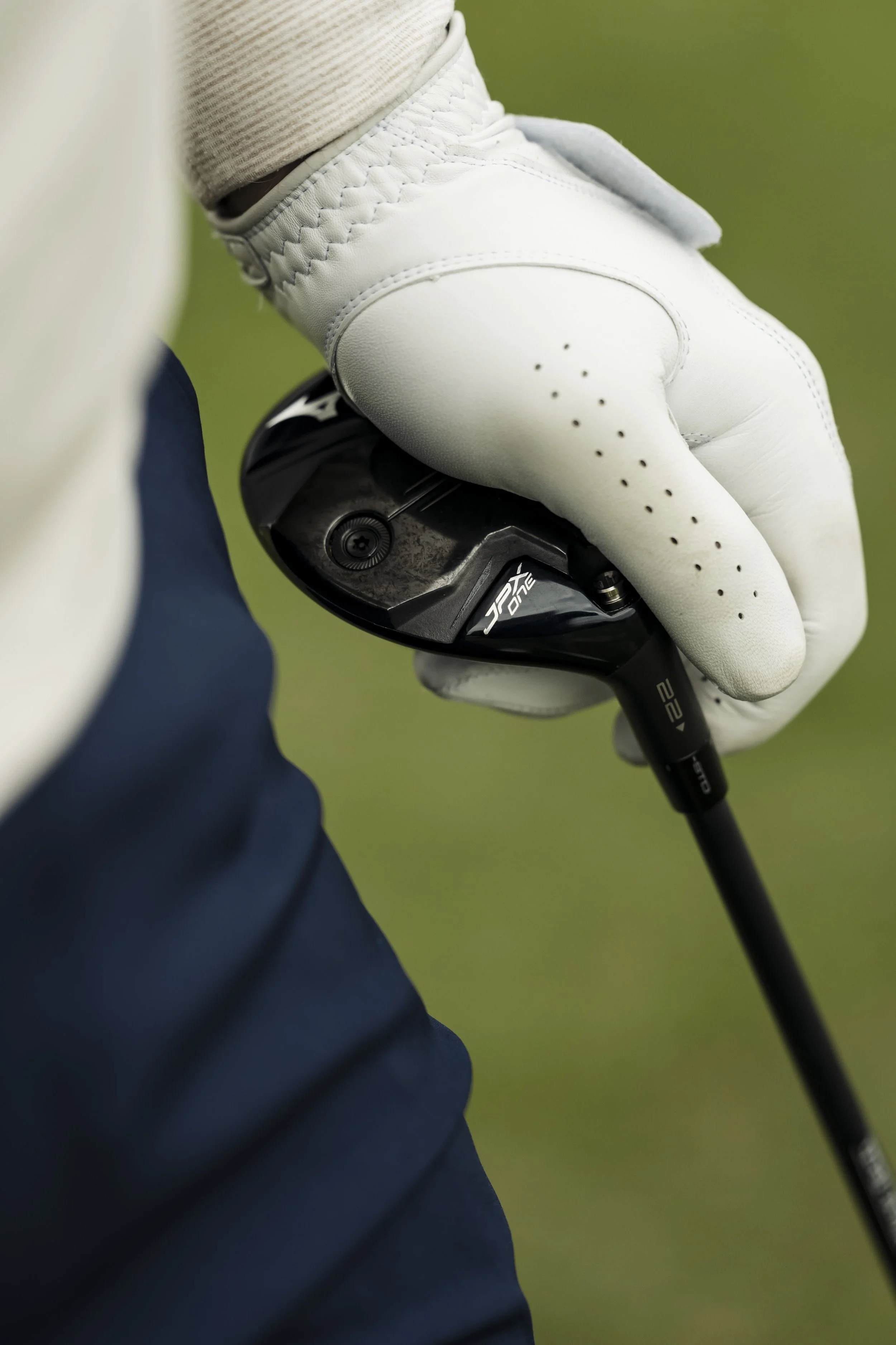 Close-up of a golfer wearing a white golf glove holding a golf club with a green field background.