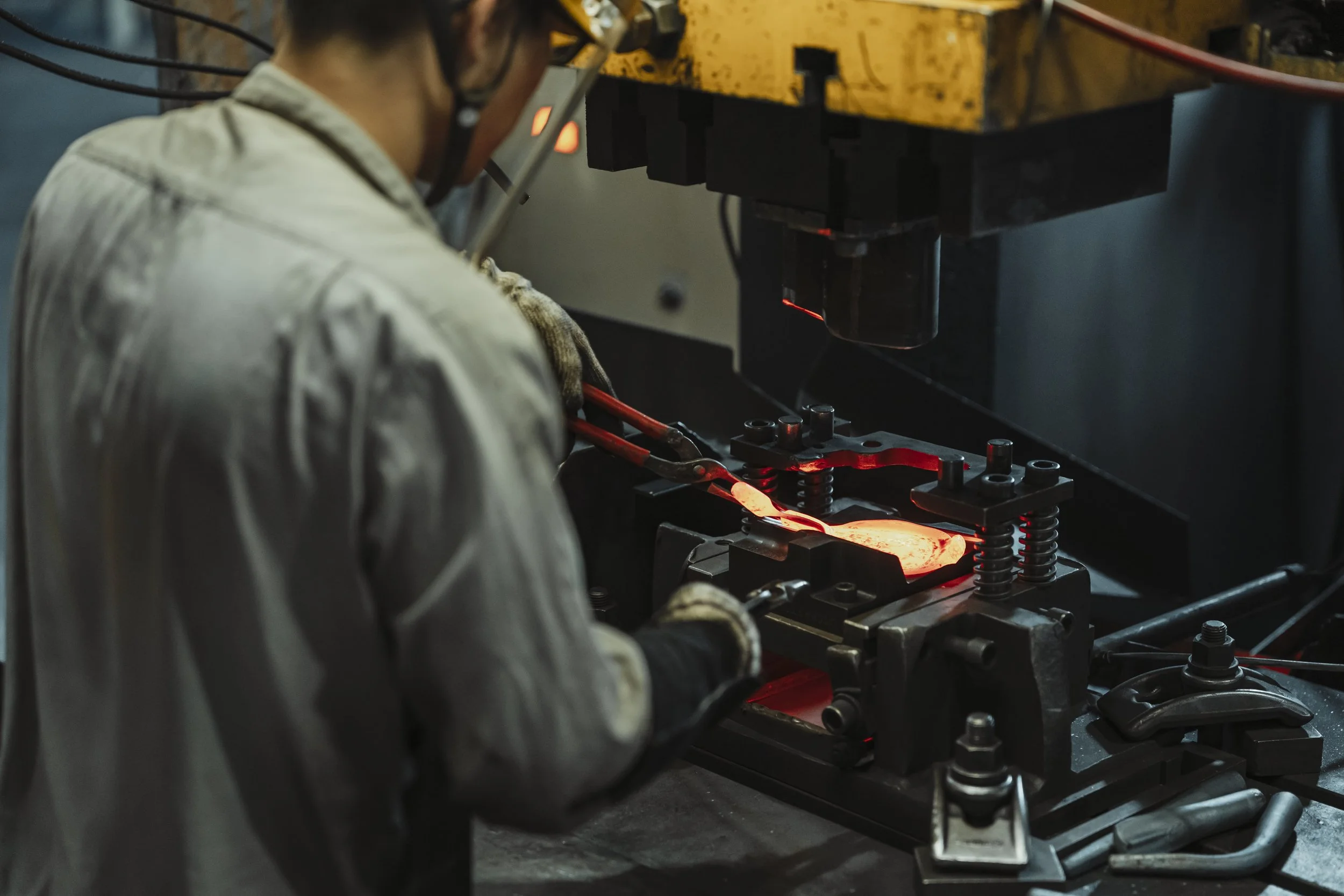 A blacksmith using tools to shape hot metal at an industrial forge.