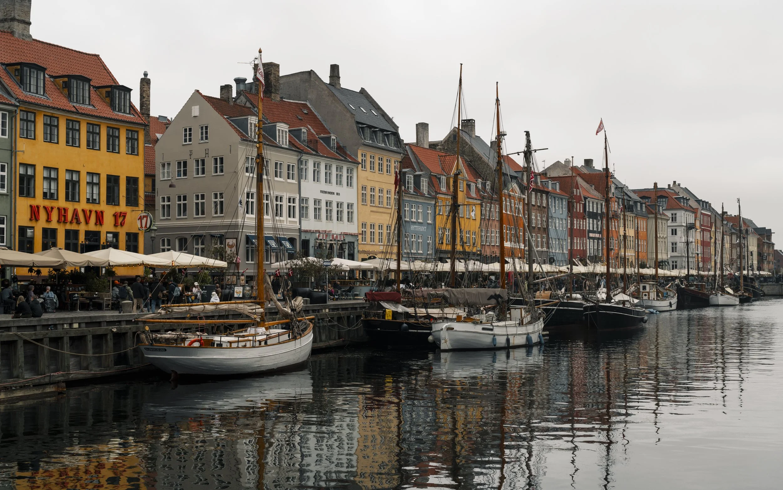 Colorful buildings along a waterfront with boats docked at a pier and people walking along the promenade.