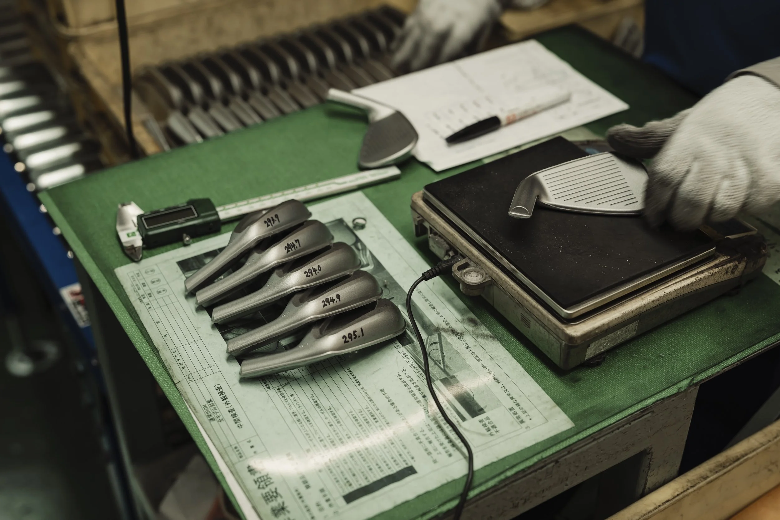Golf clubs, a golf club measuring device, and a golf club face on a scales on a green table at a golf shop or repair shop.