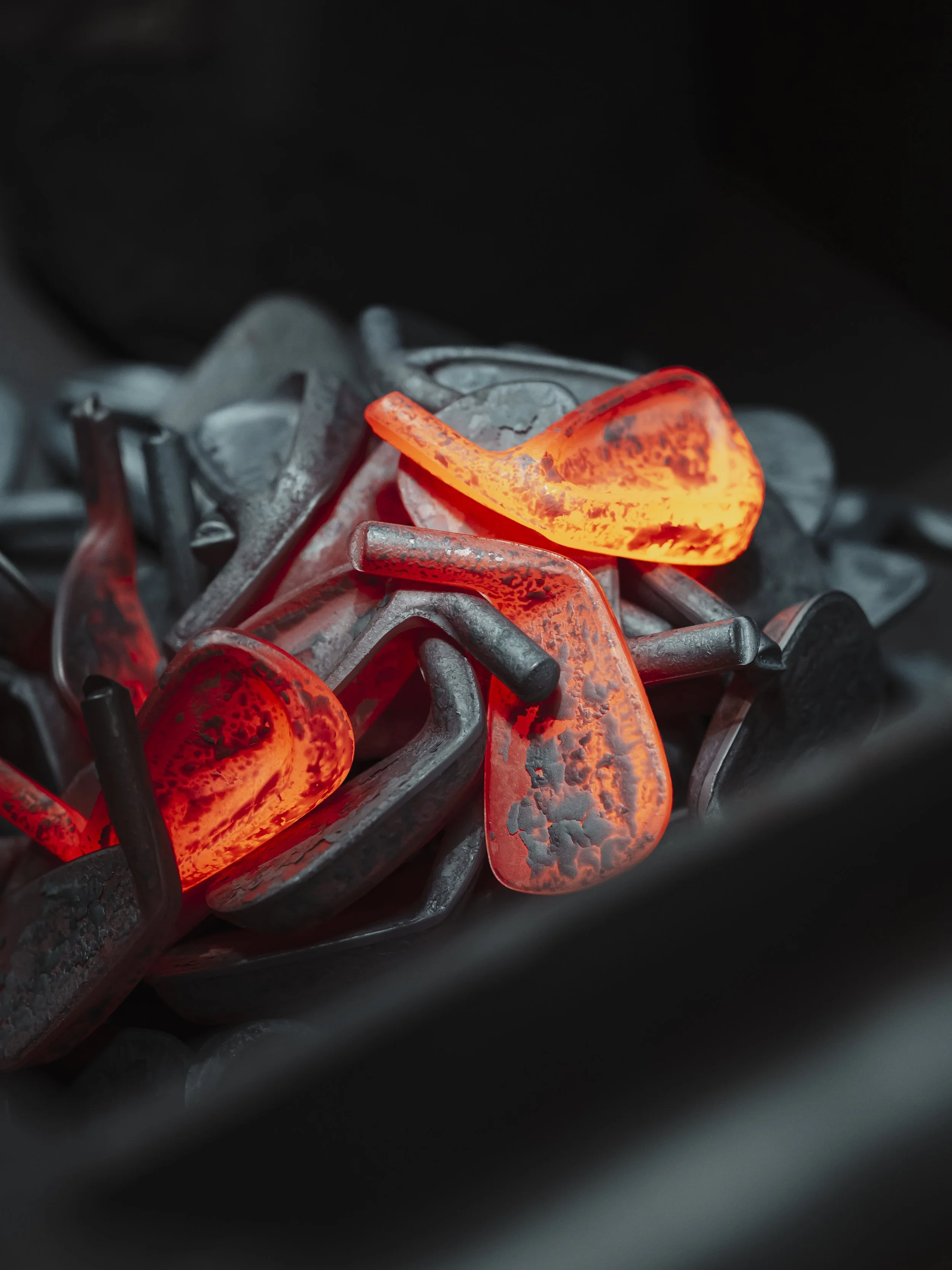 A pile of glowing, heated metal hooks or clasps with a bright orange and red glow, resting on a dark surface.