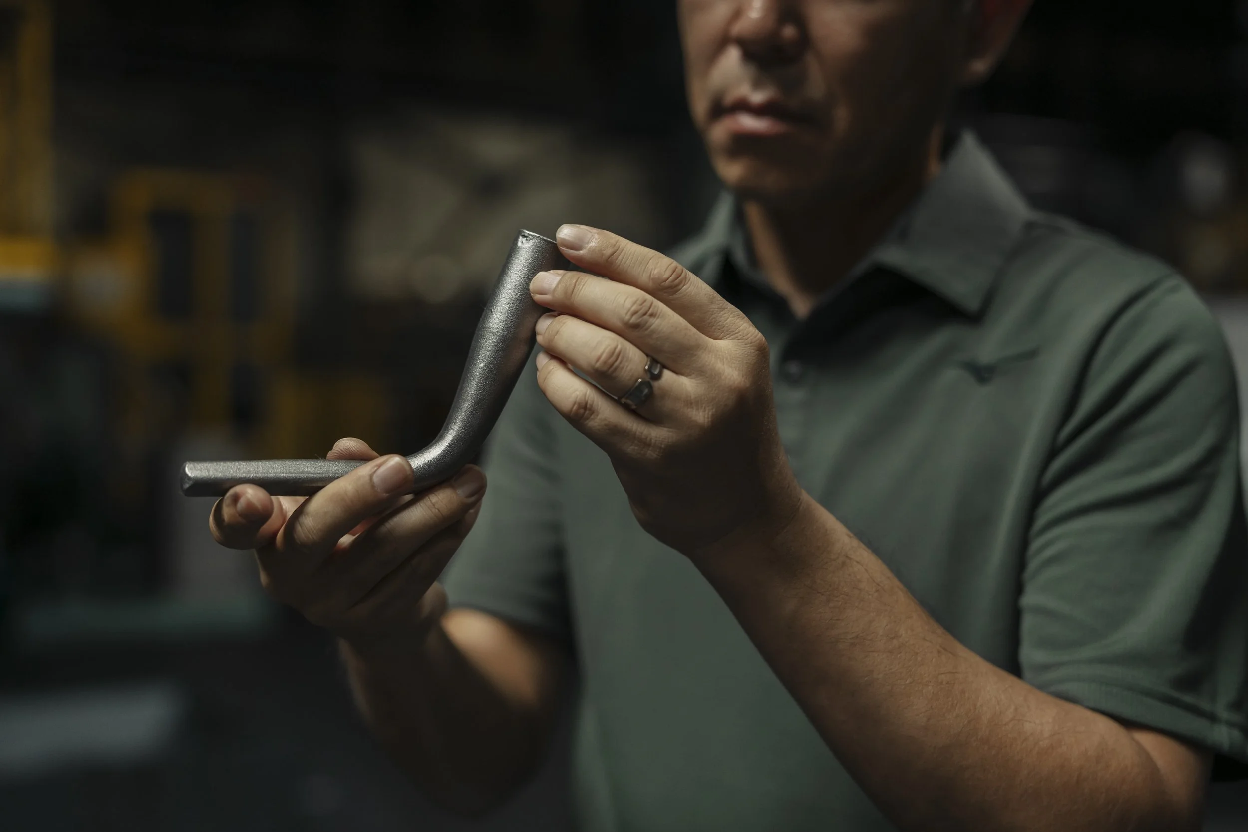A man inspecting a metal L-shaped part in a workshop or factory setting.