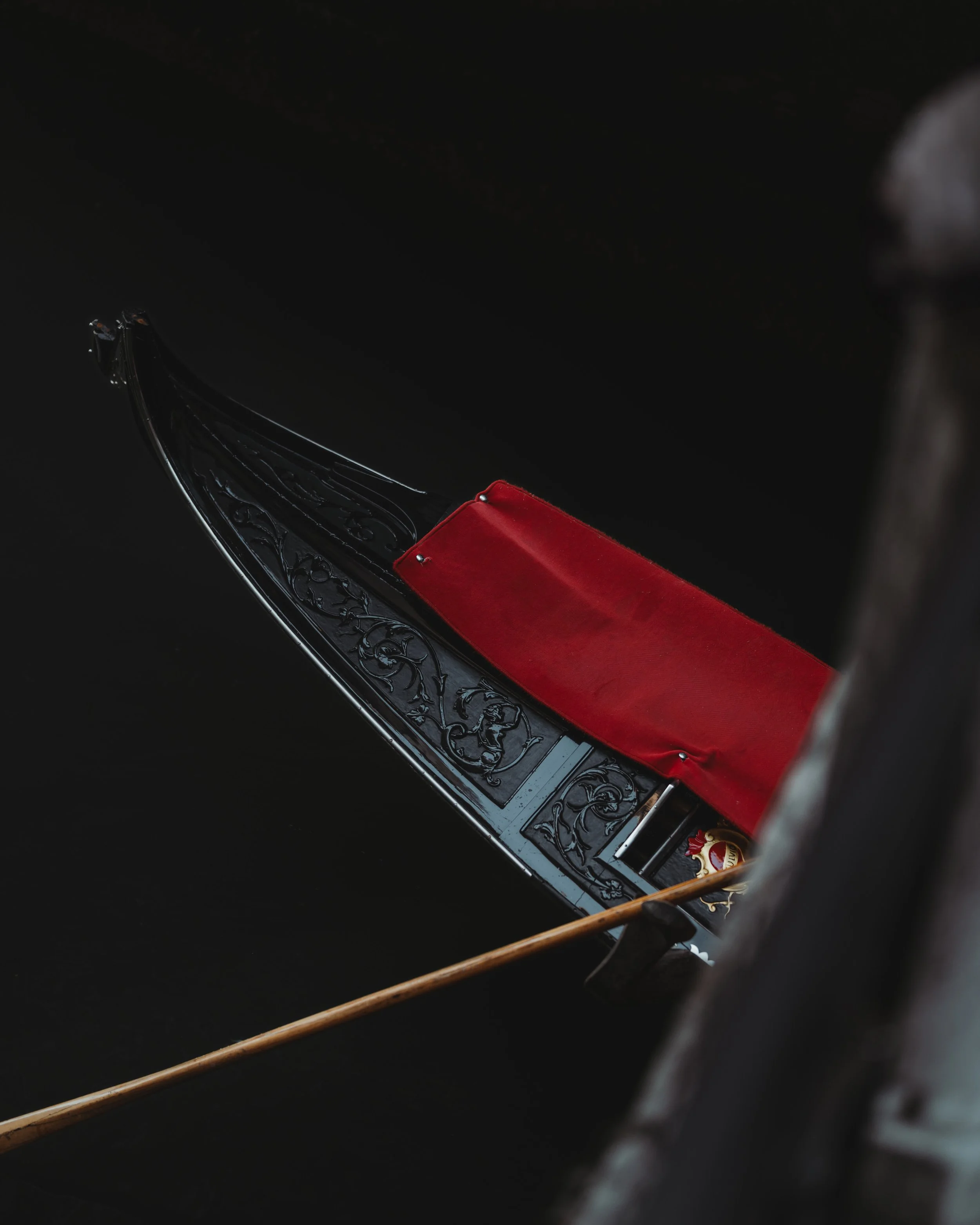 Gondola with ornate black decoration and red seat cushion floating on dark water in Venice, Italy.