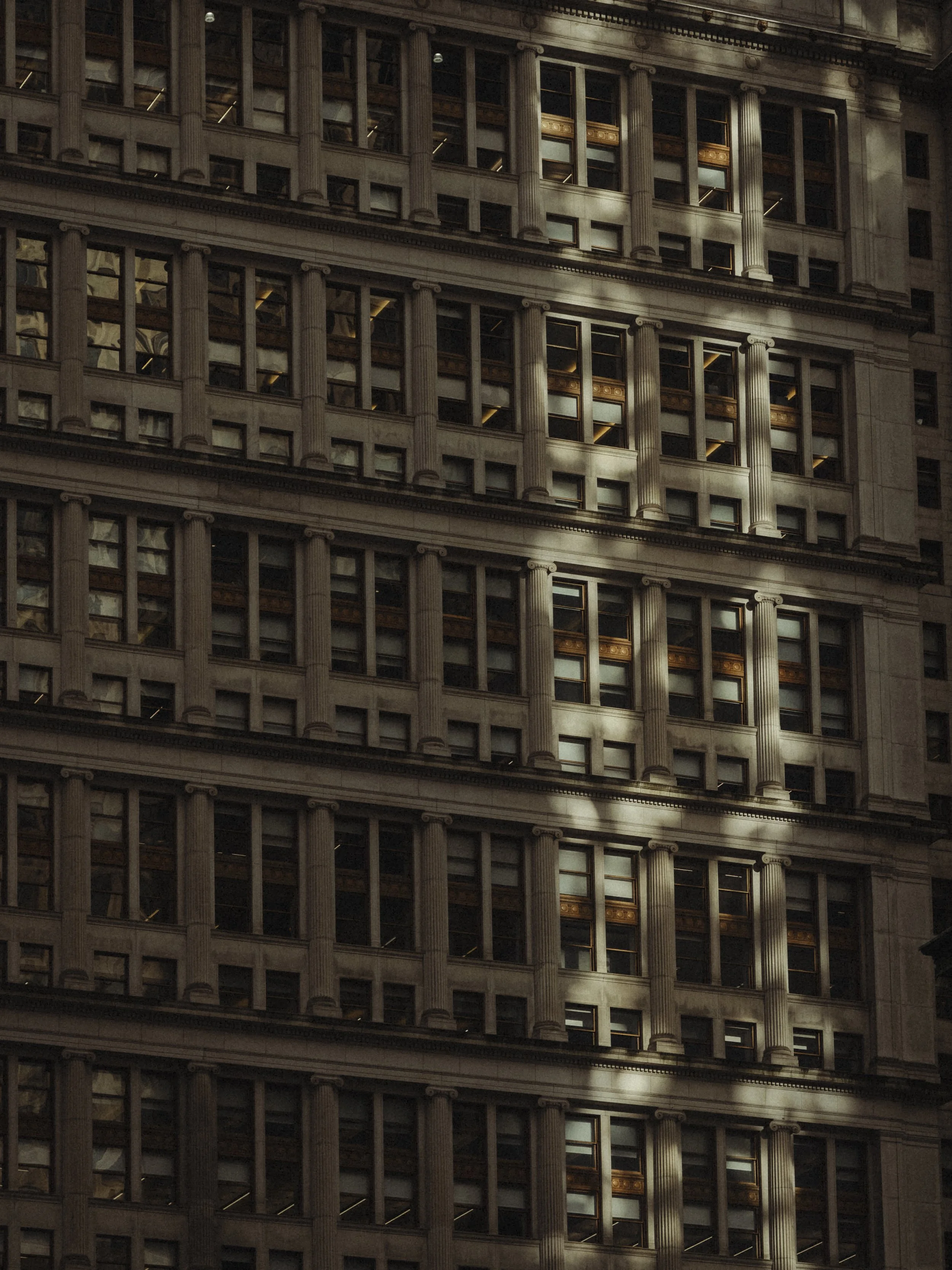 Close-up of a tall office building with multiple windows and decorative columns in a classical architectural style, illuminated by sunlight.