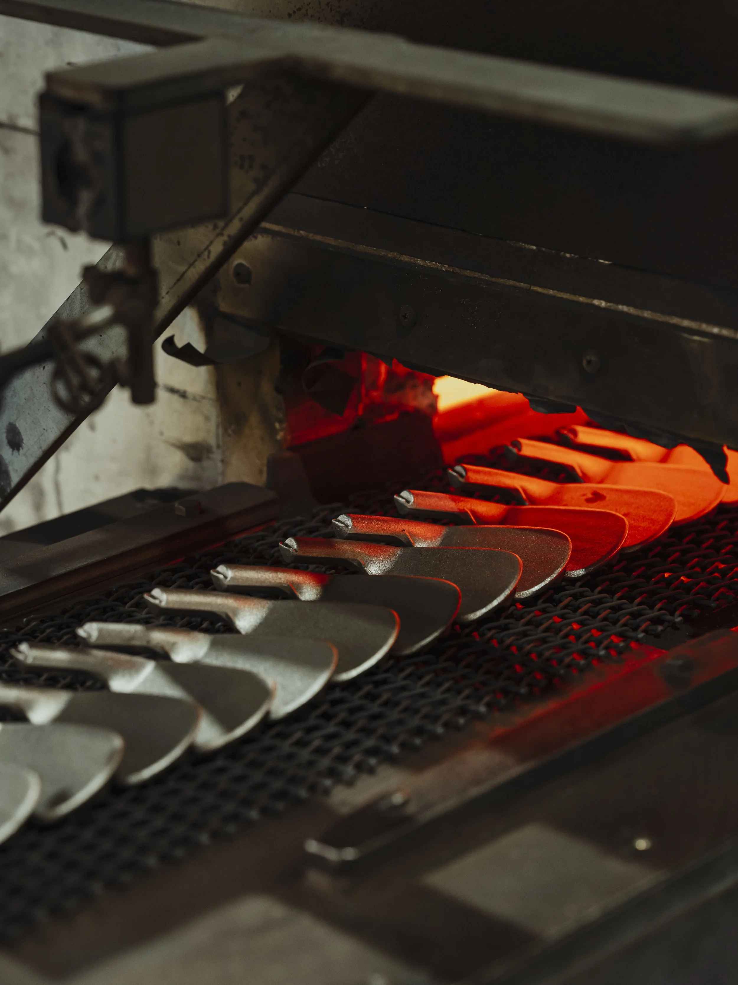 A furnace with several metal golf club heads being heated to forge.