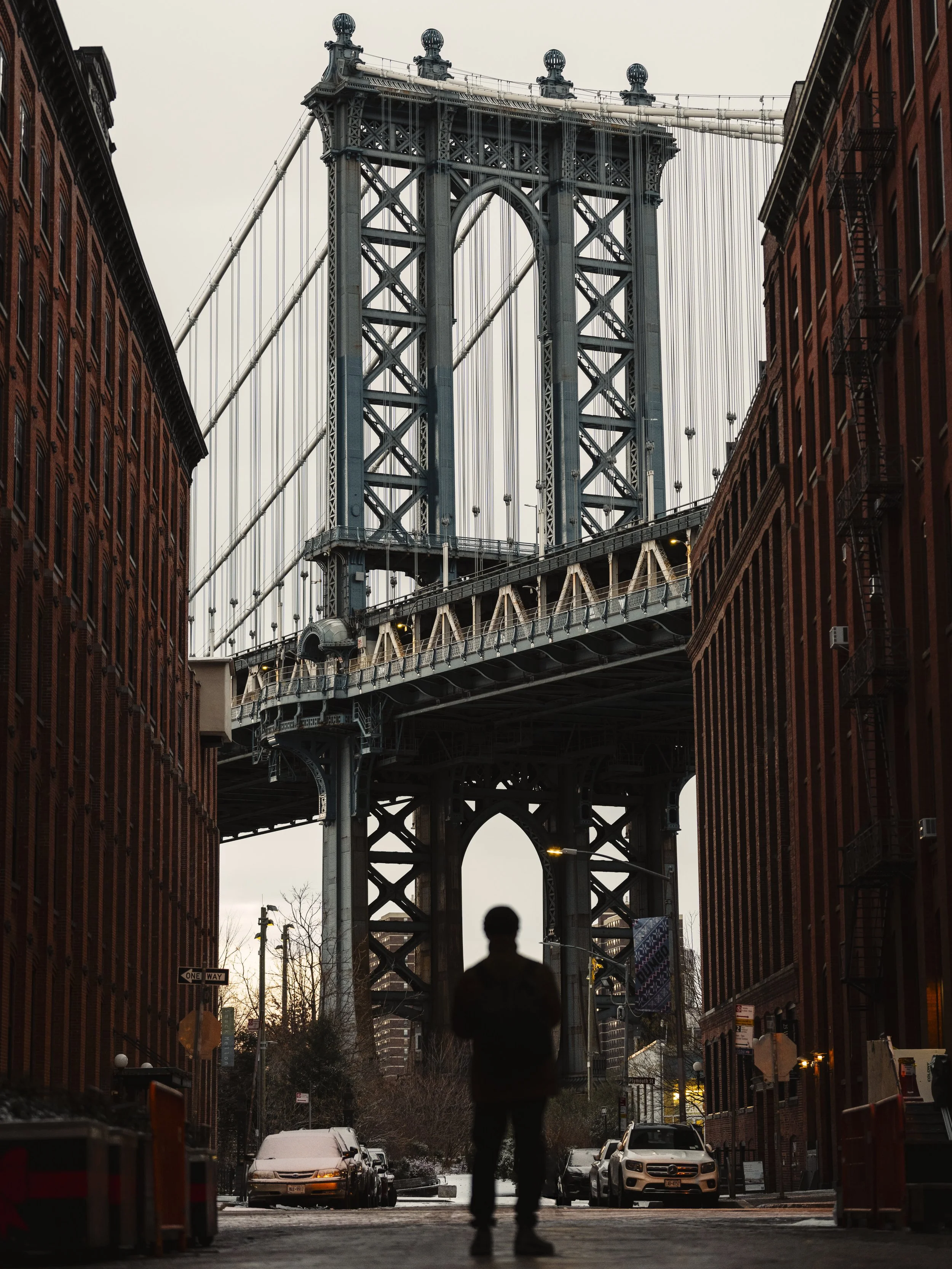 A person walking in a city street with the Brooklyn Bridge in the background.