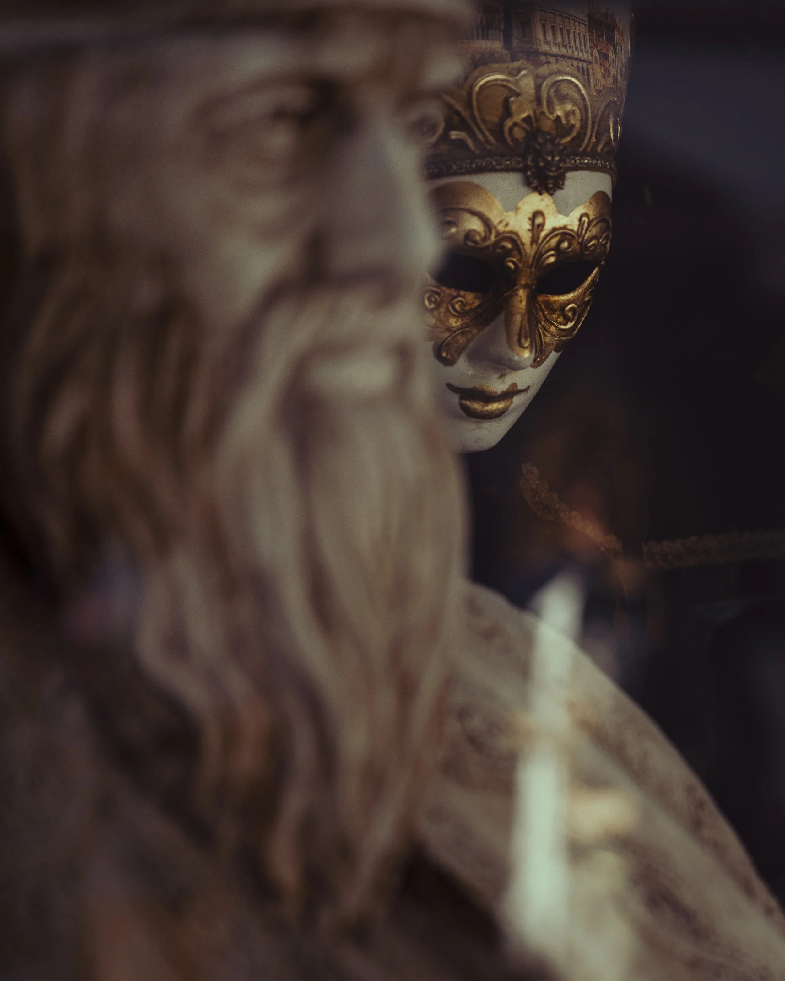 Decorative masks with one showing a face with gold accents and intricate designs, and another with a long beard, set against a dark background.
