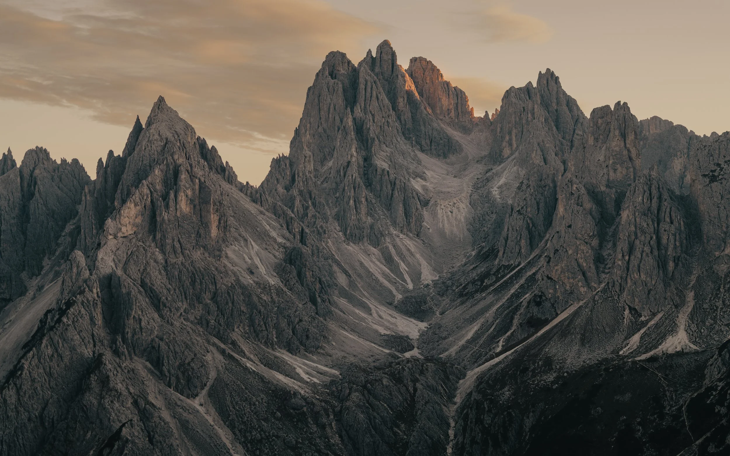Mountain range with rugged peaks during sunset, no snow on the mountains, cloudy sky.