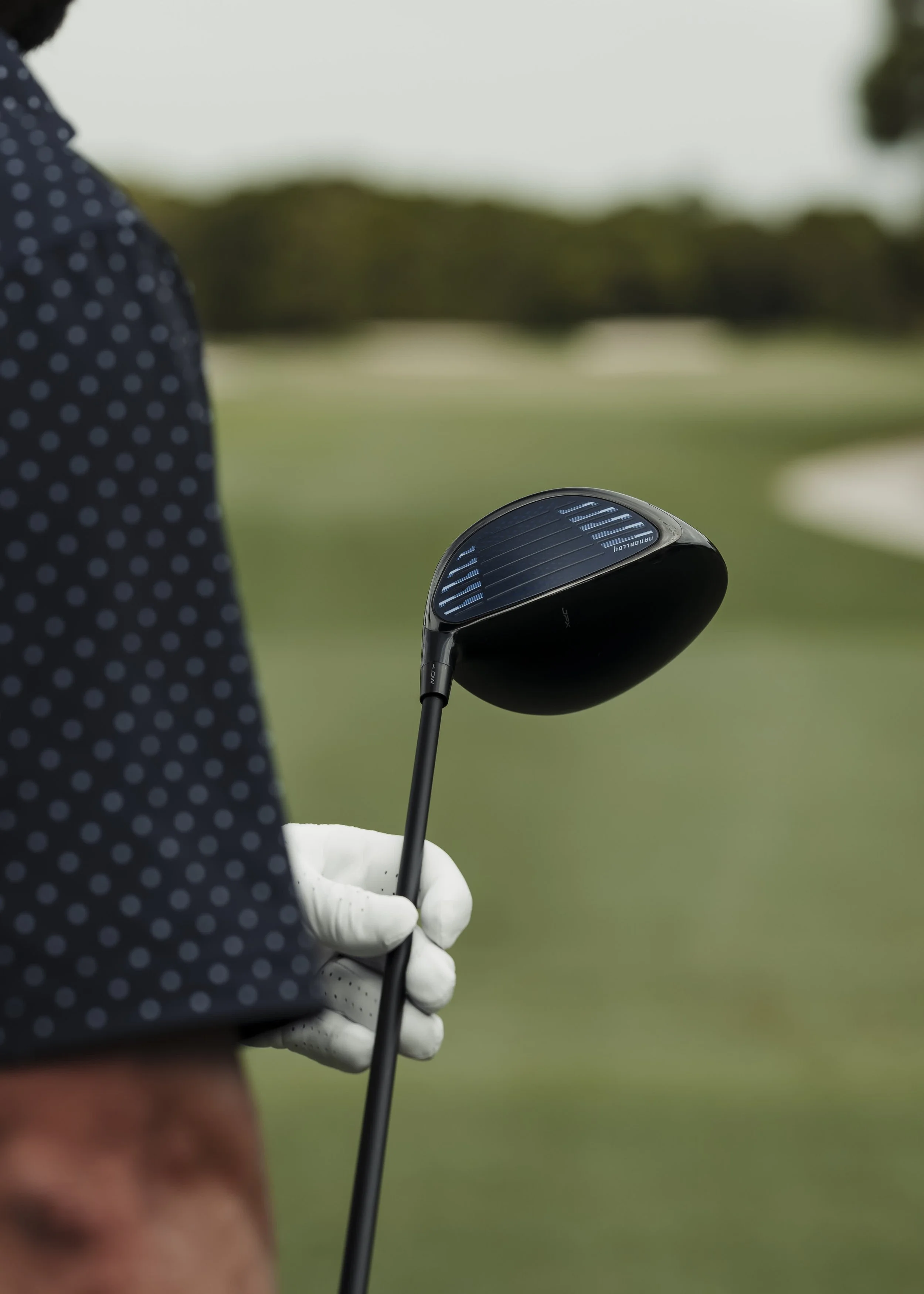 Close-up of a person holding a golf club on a golf course, with a blurred background.