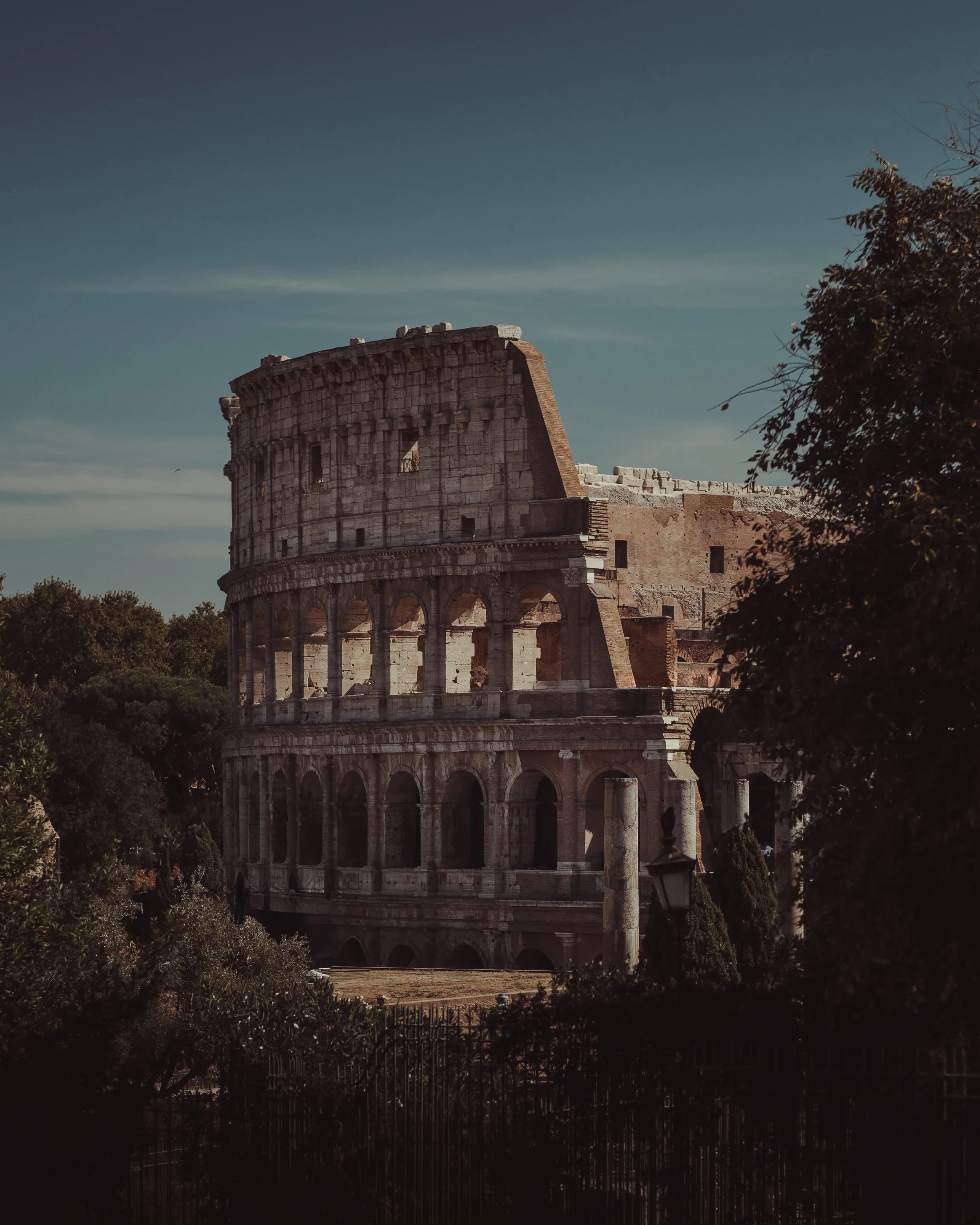 Photograph of the ancient Roman Colosseum in Rome, Italy, showing its iconic arches and partially ruined structure during daytime with clear skies.