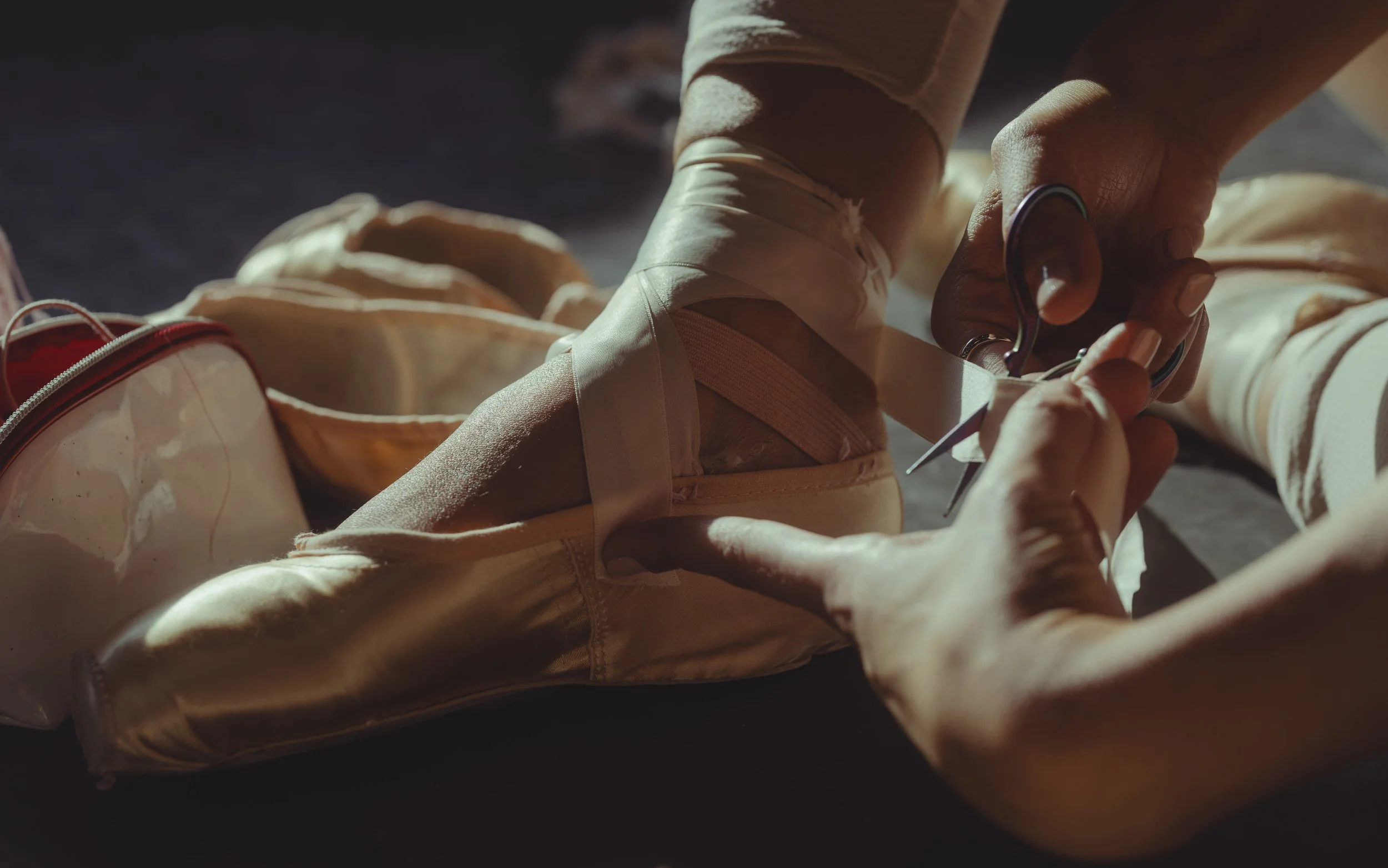 A person using scissors to cut a beige fabric or clothing item on a dark surface, with related items nearby.