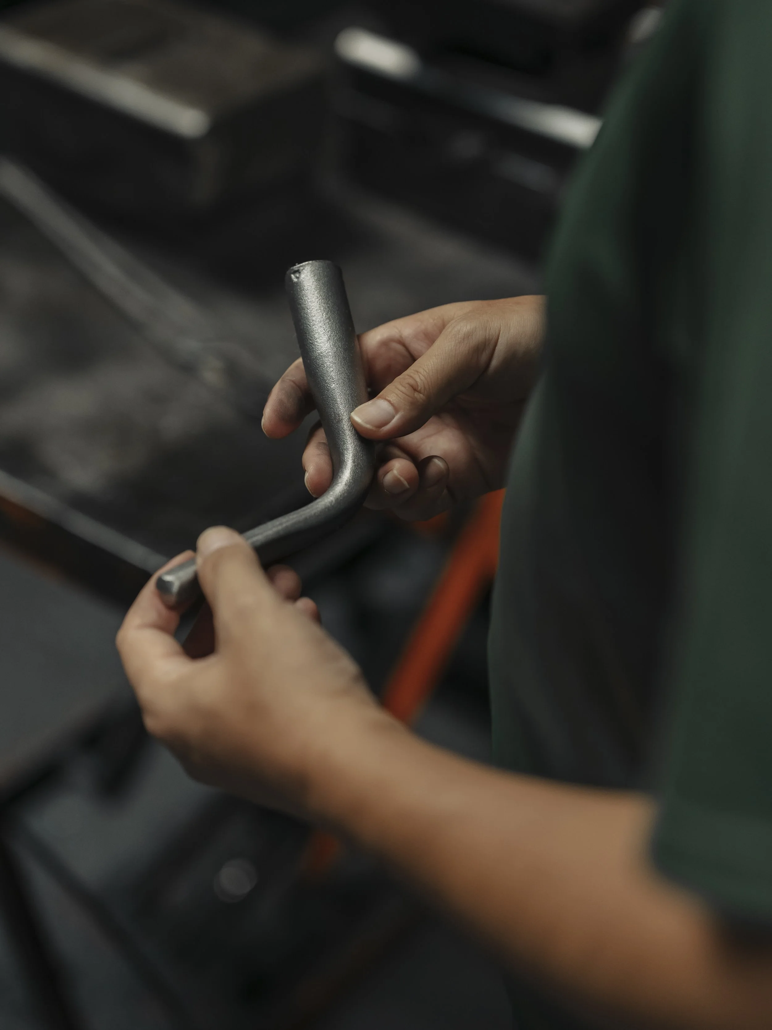 Person holding a metal L-shaped tool, possibly a wrench or Allen key, in a workshop or industrial setting.
