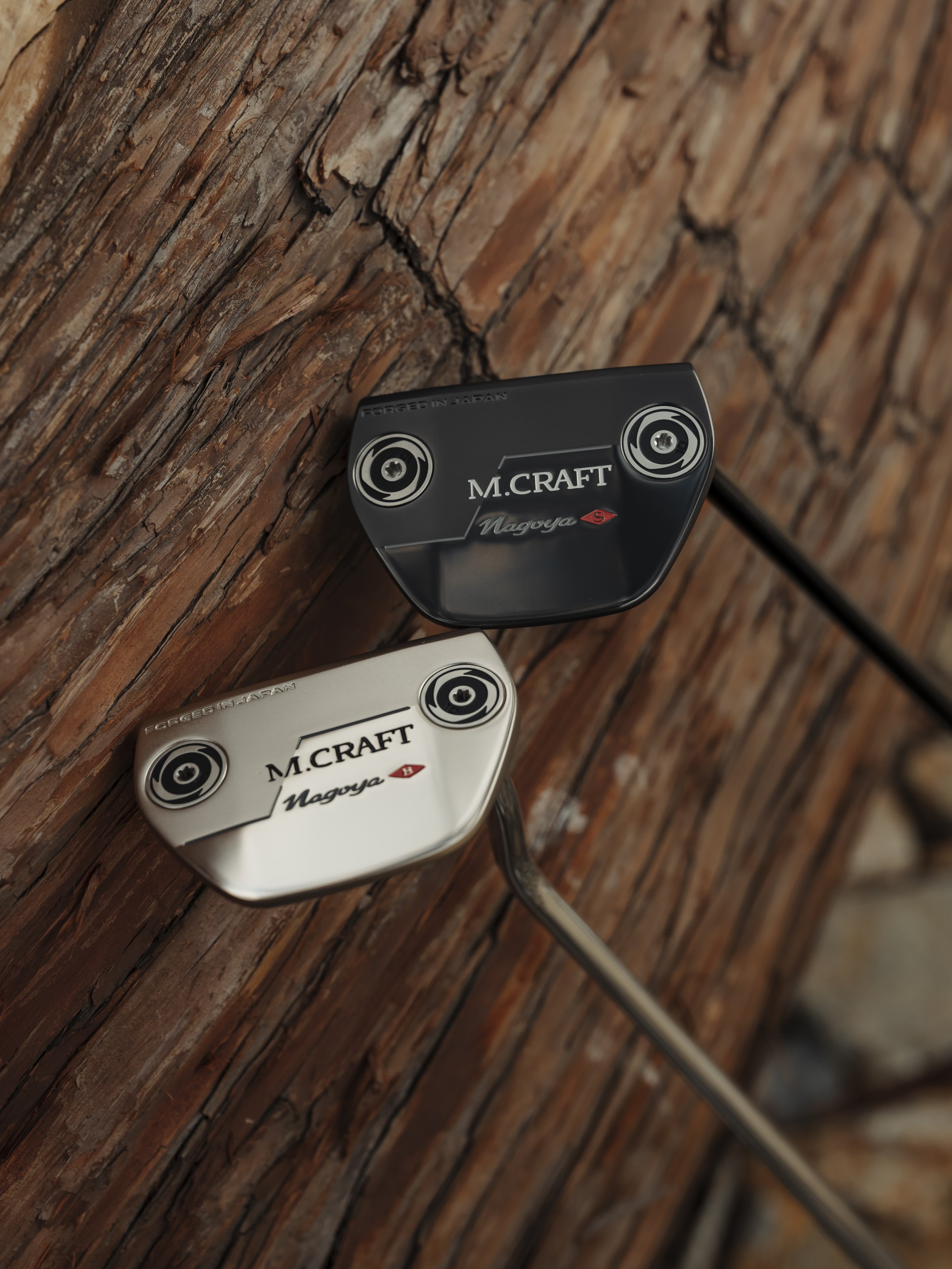 Close-up of two golf club putters, one black and one metallic silver, leaning against a textured wooden surface.