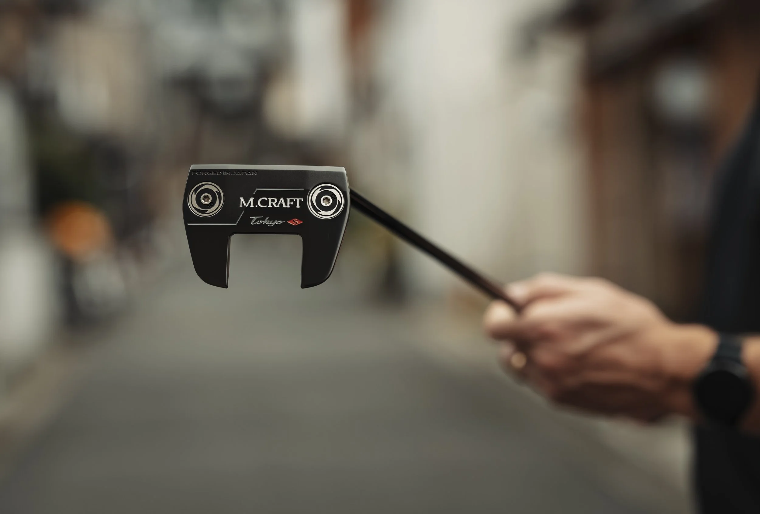 Close-up of a golf club head held by a person on a blurred street background.