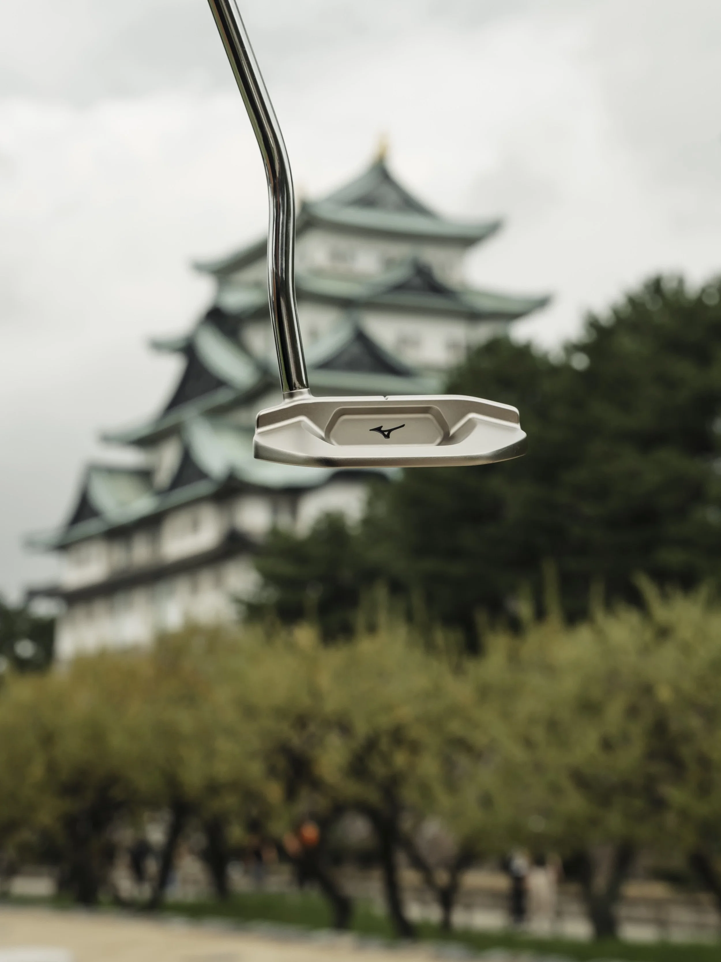 Close-up of a golf putter with a traditional Japanese castle in the blurry background.