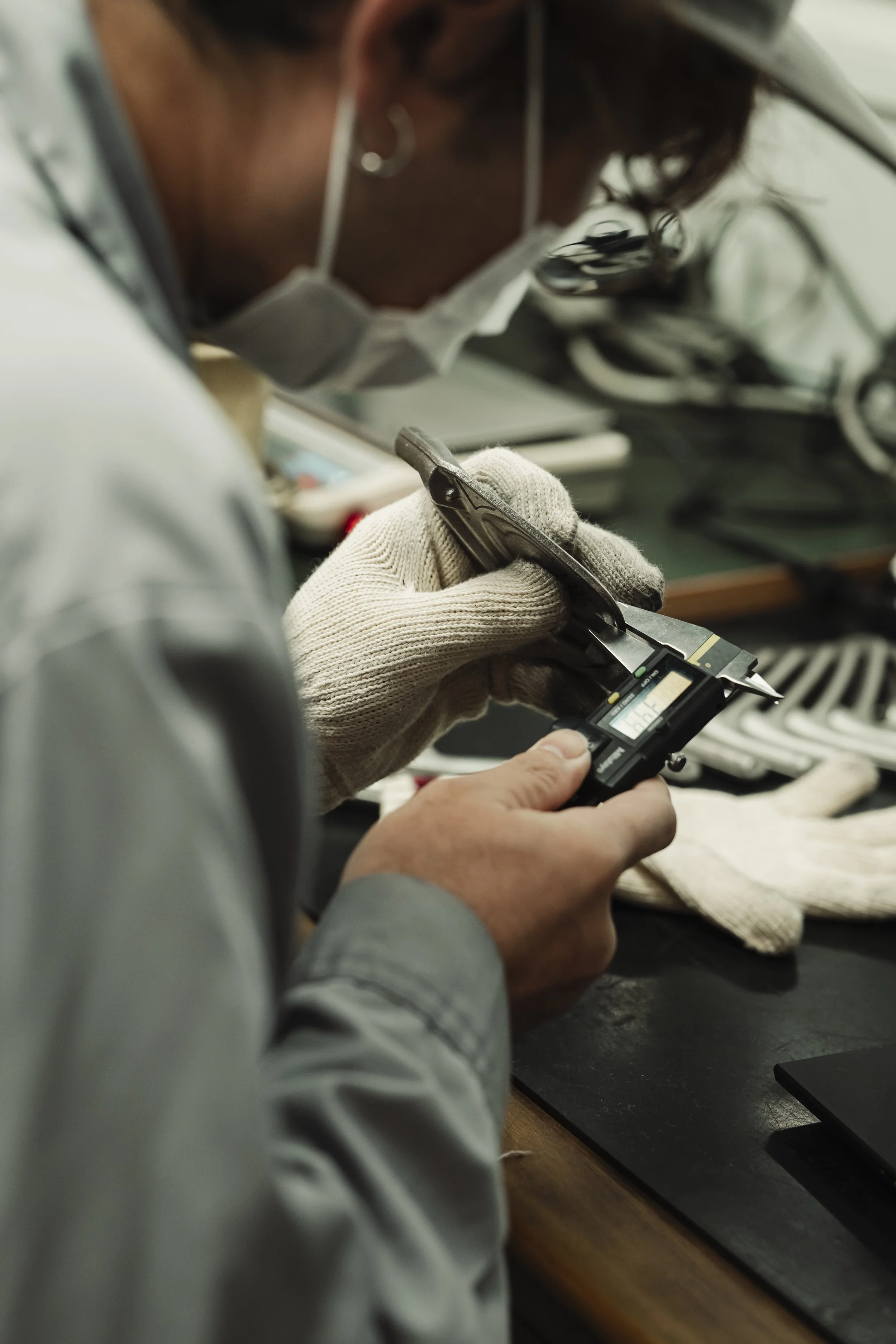 A person wearing a mask, gloves, and glasses is working with precision tools at a workbench.