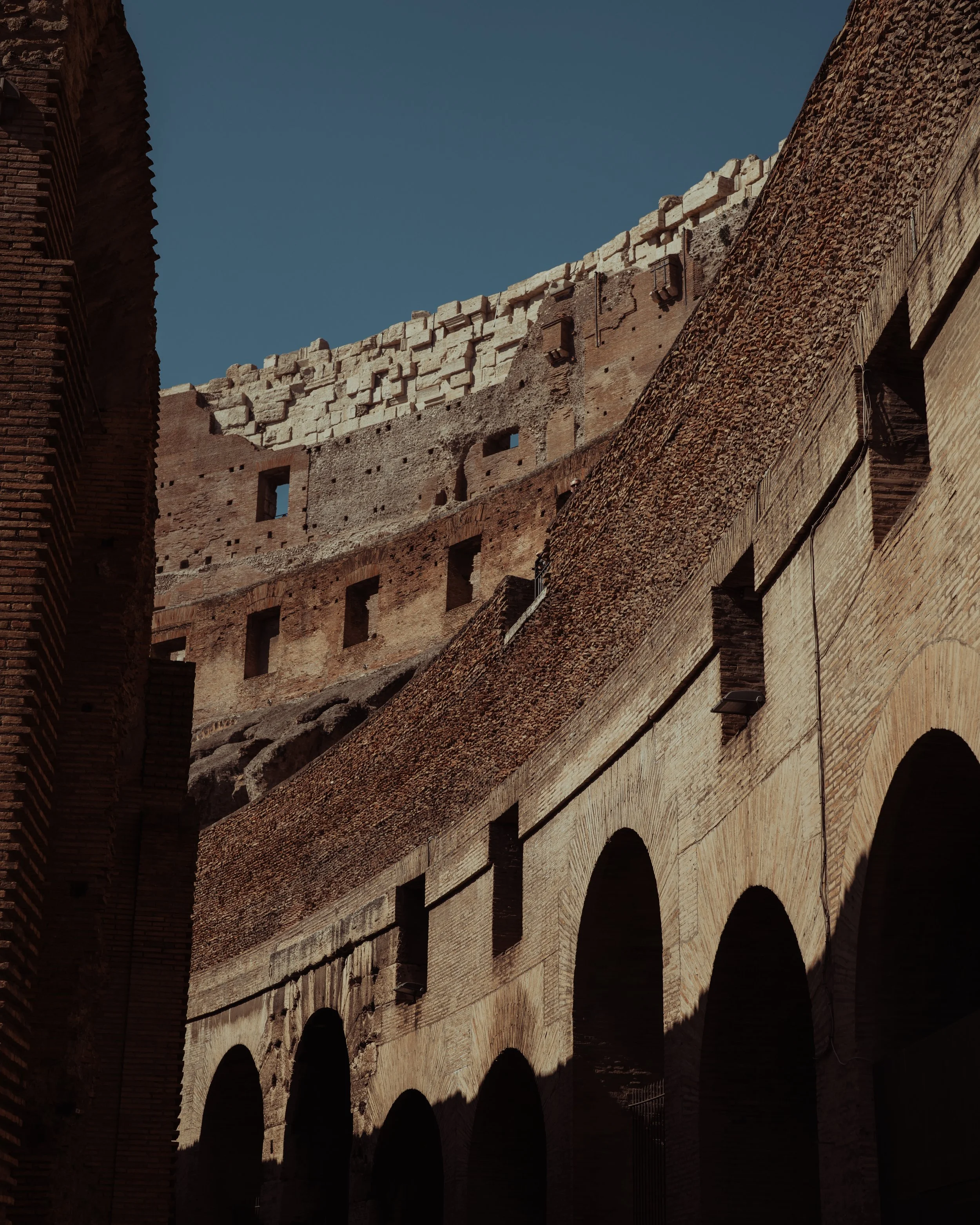 Close-up of the interior walls and arches of the Colosseum in Rome, Italy, with sunlight casting shadows on the brick and stone structures.